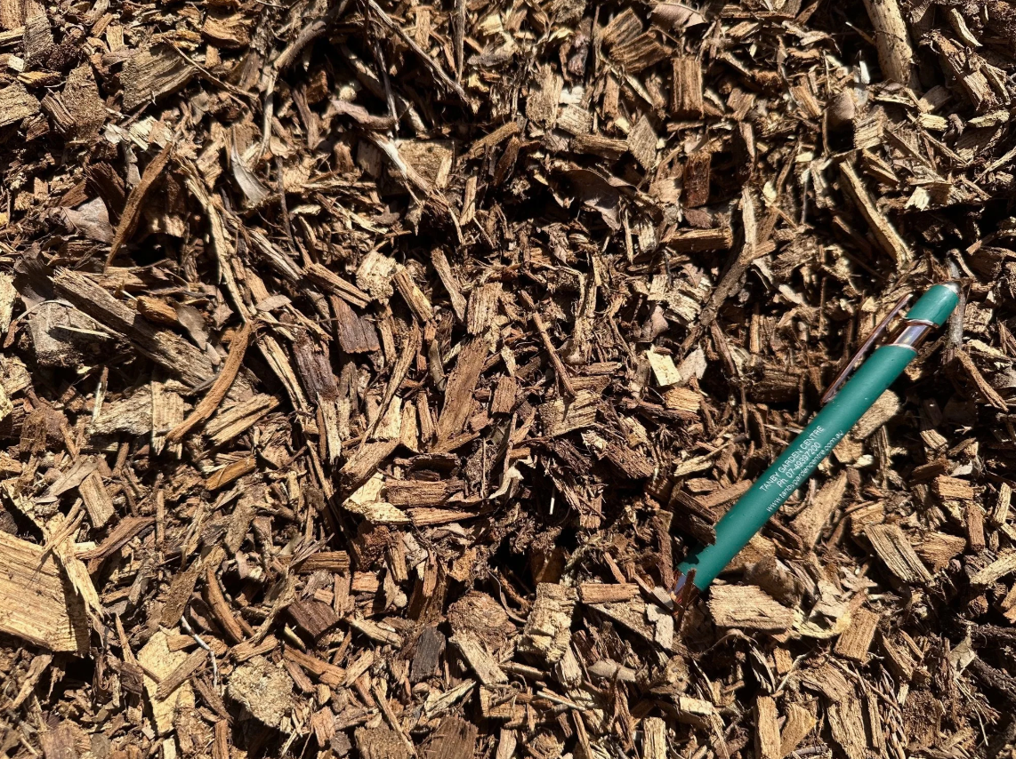 A green pen lying on a bed of brown wood chips.