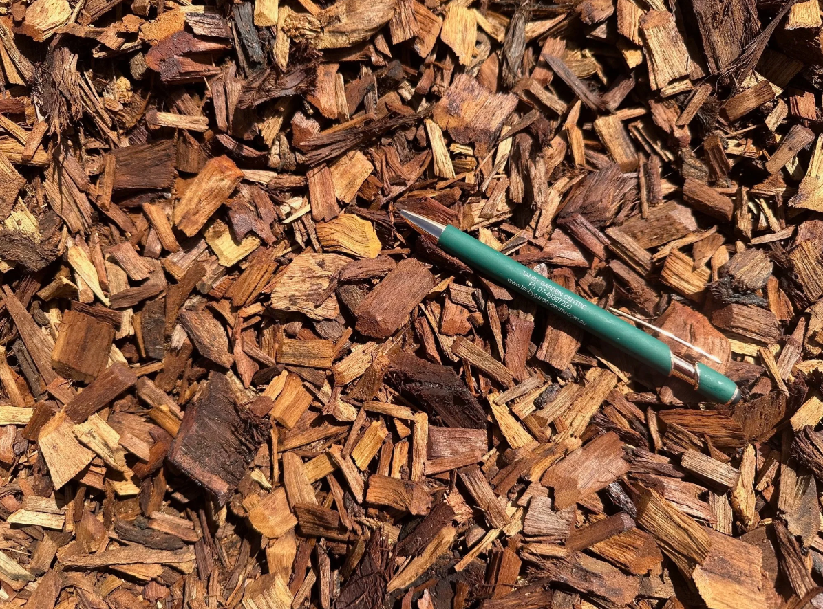 A green pen resting on brown wood mulch ground.
