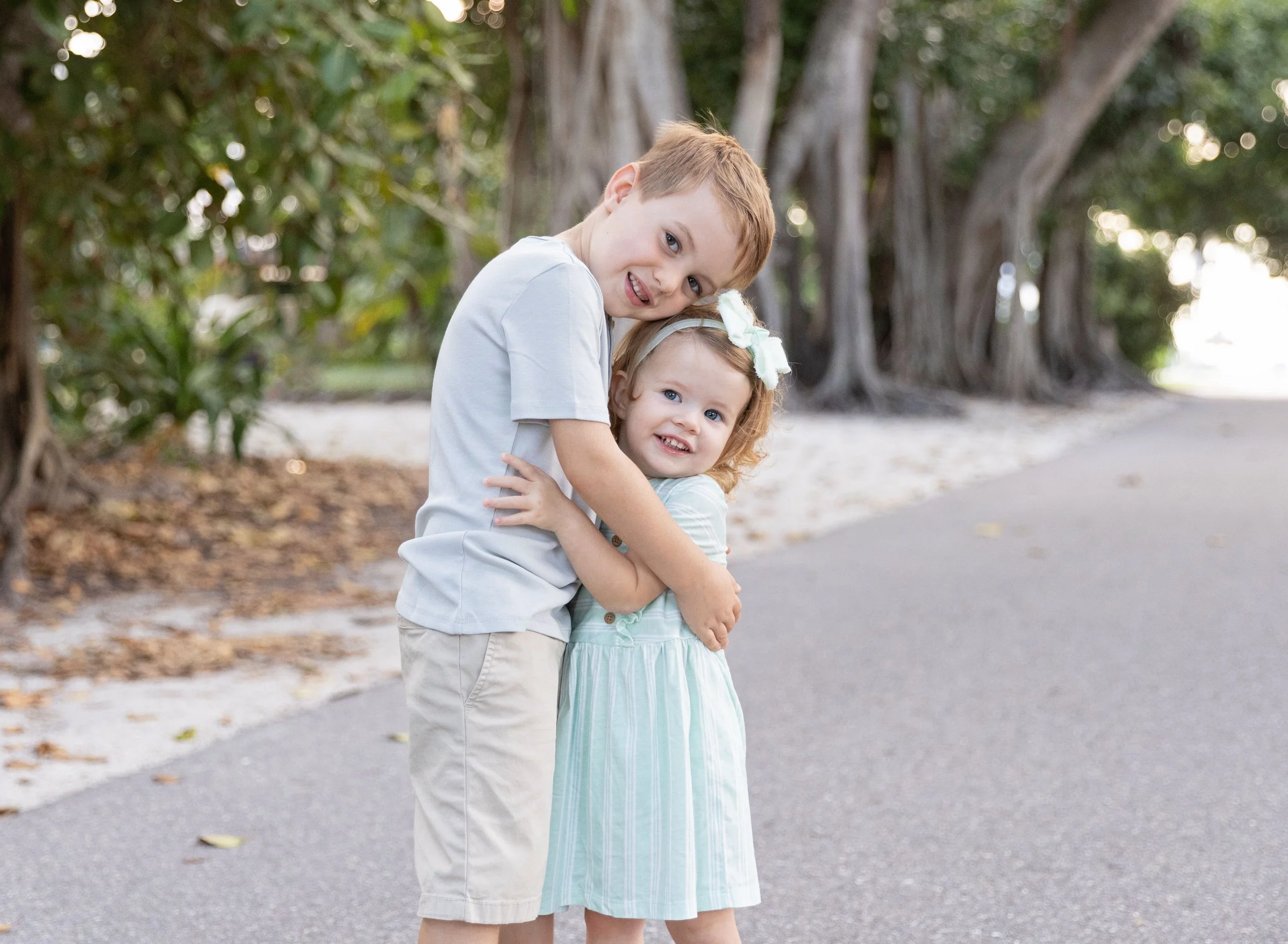 Big brother hugging little sister by banyan trees at the beach in Venice FL