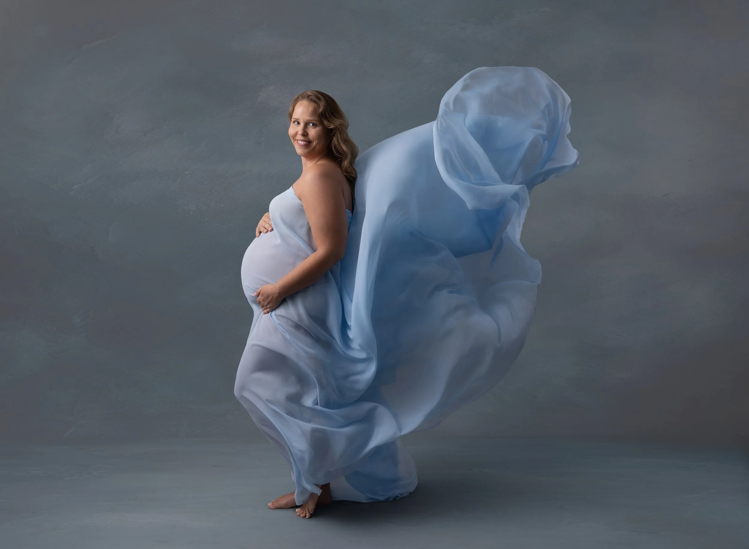 Pregnant mom in flowing blue fabric in Port Charlotte photo studio.