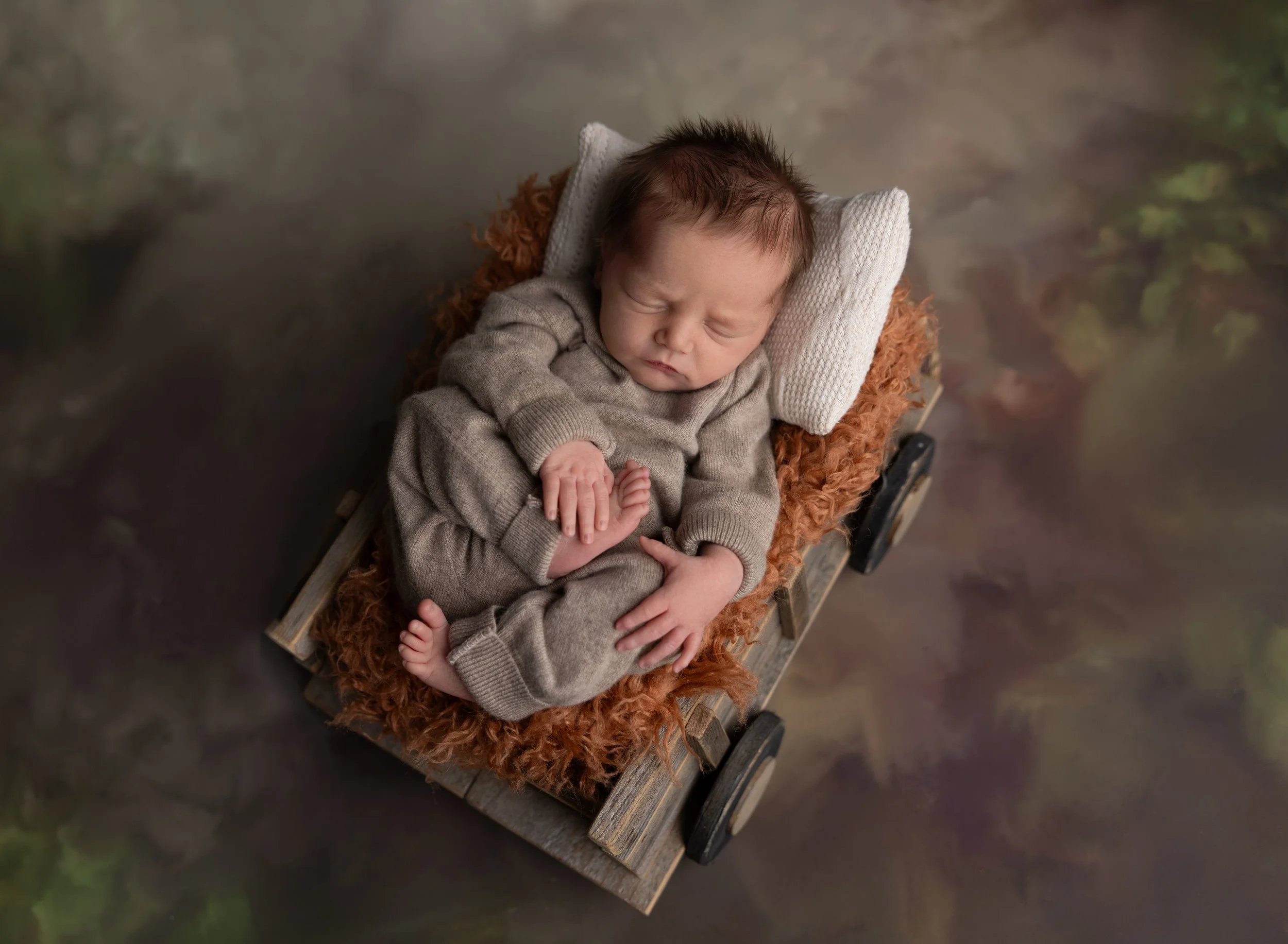 Newborn boy in wagon prop holding his foot in Venice, FL photo studio.