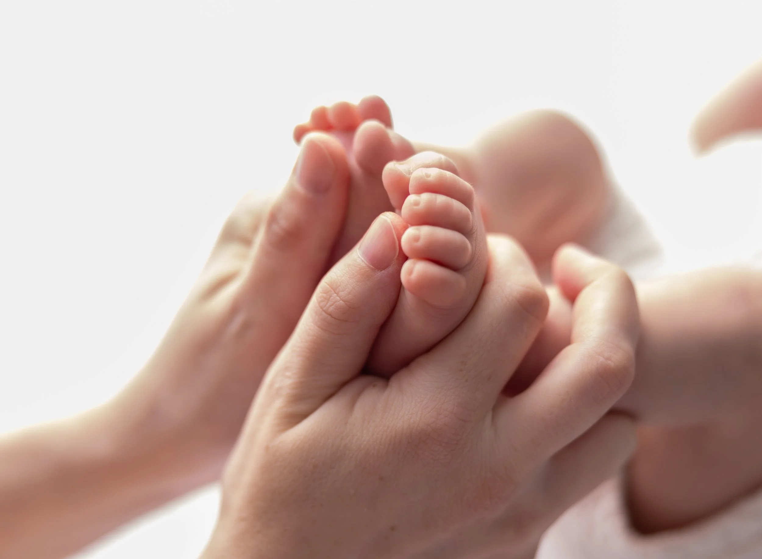 Backlit image of mom holding baby's feet in Cape Coral photo studio. 