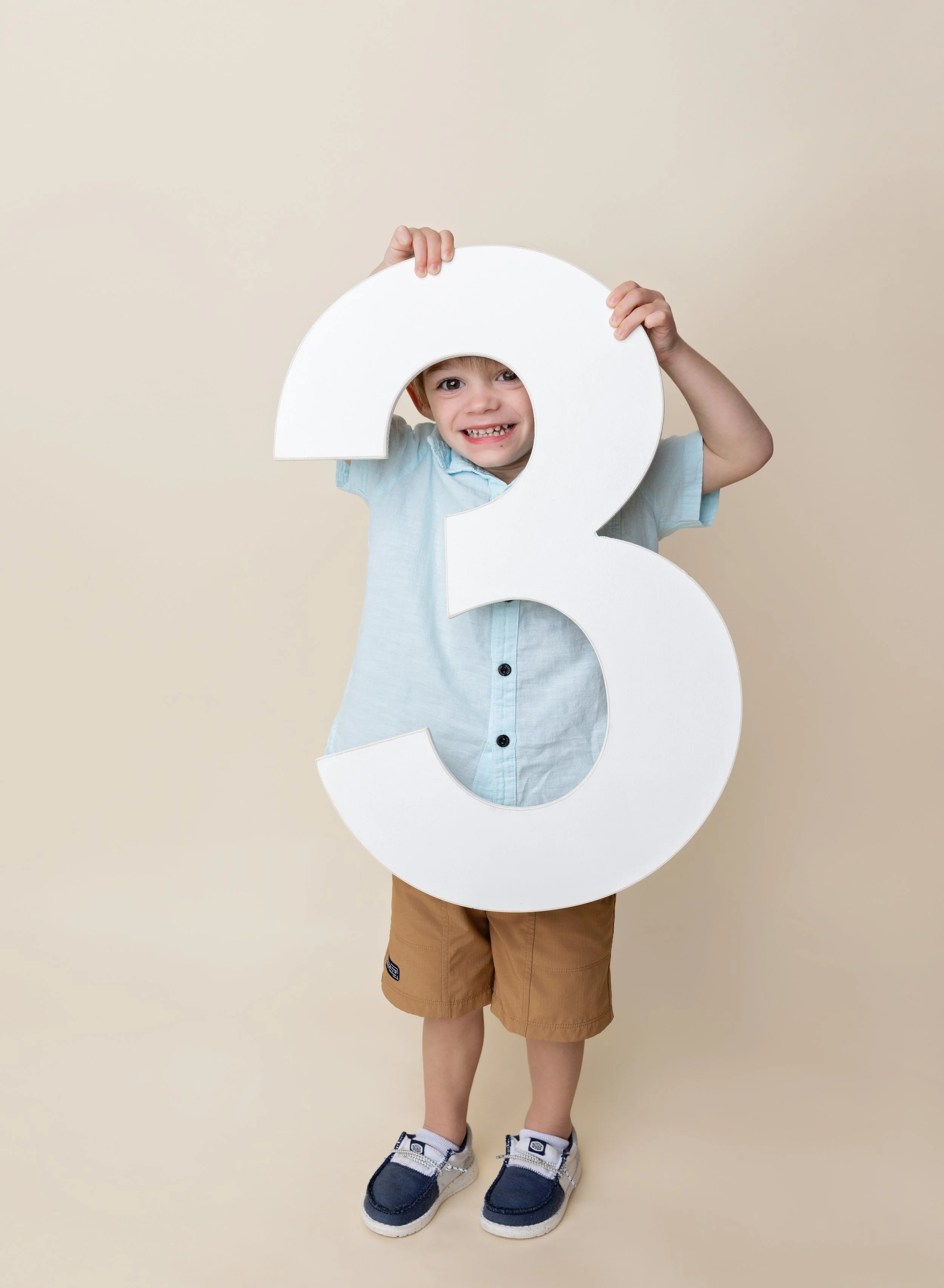 Three year old boy holding a number three prop on cream. backdrop Sarasota, FL