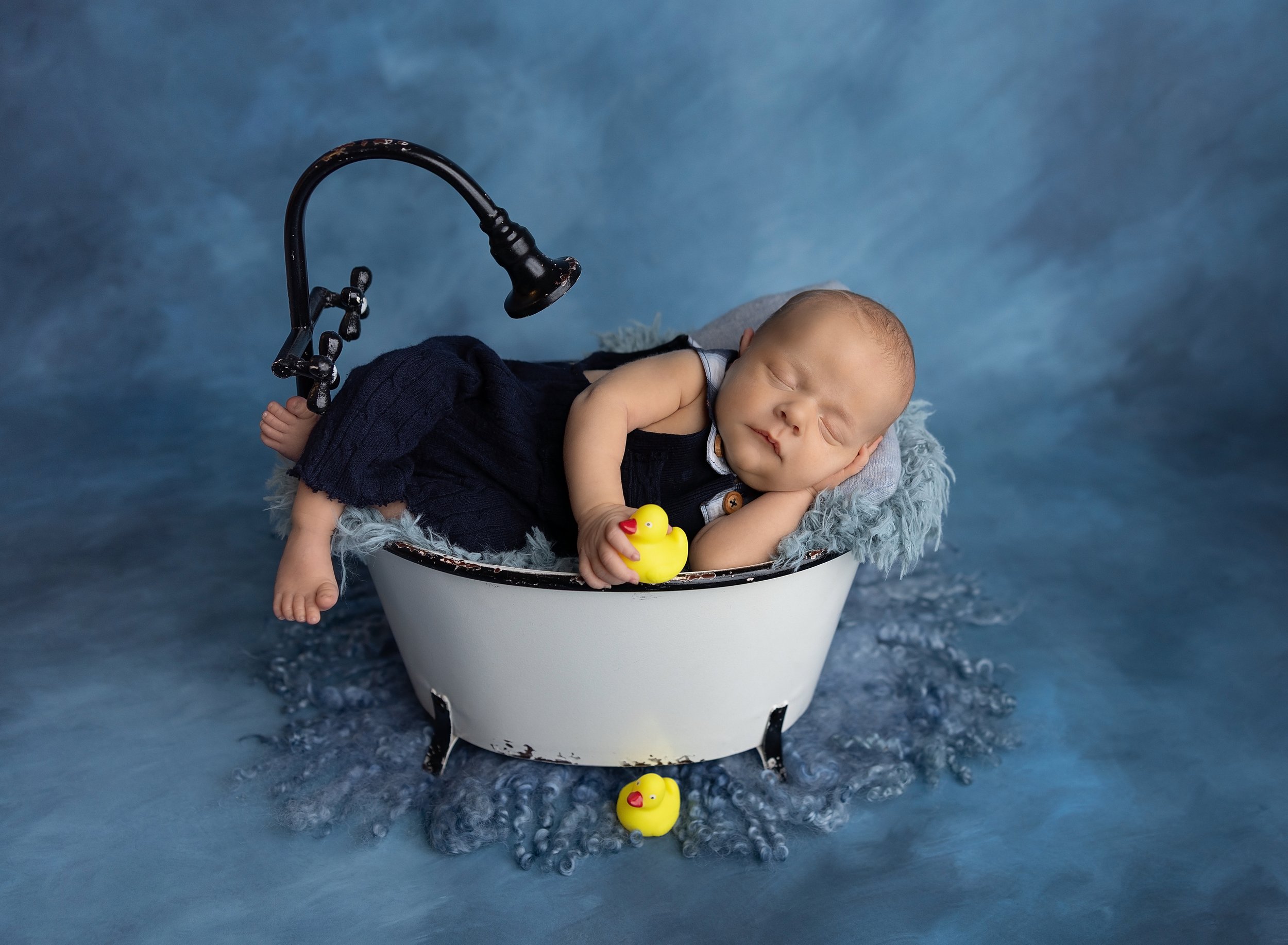 Newborn boy in bathtub holding rubber ducks in North Port, FL photo studio.