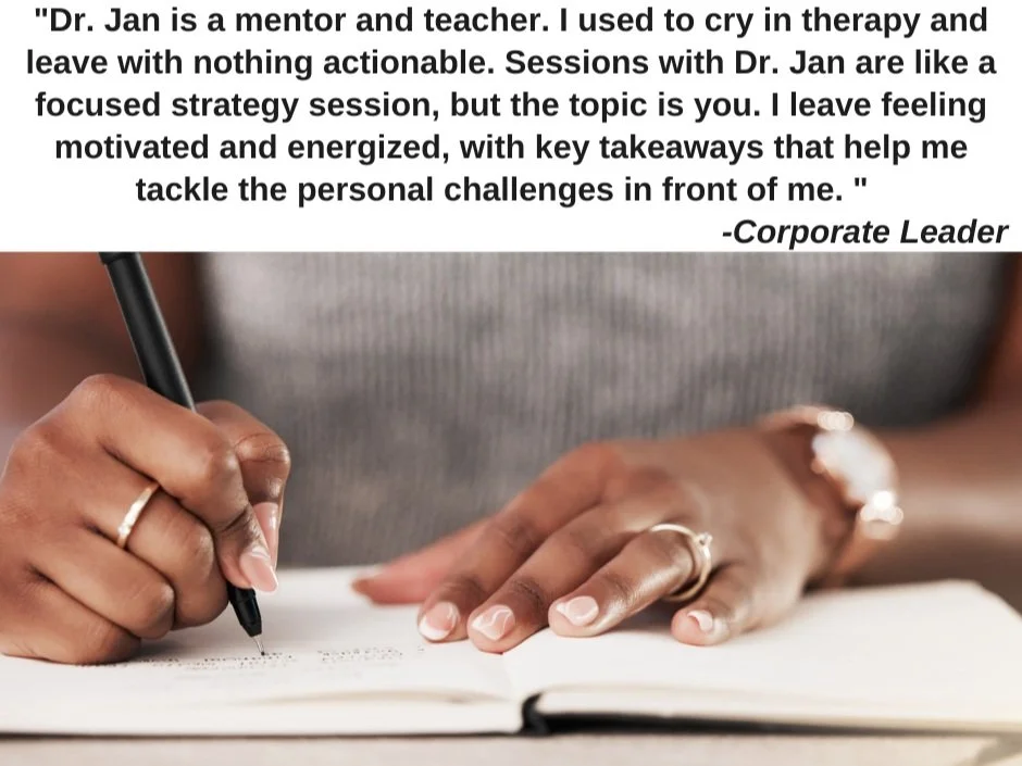 A person holding a black pen is writing in a notebook, with their other hand resting on the page, wearing rings and a watch. The person is wearing a gray sweater.