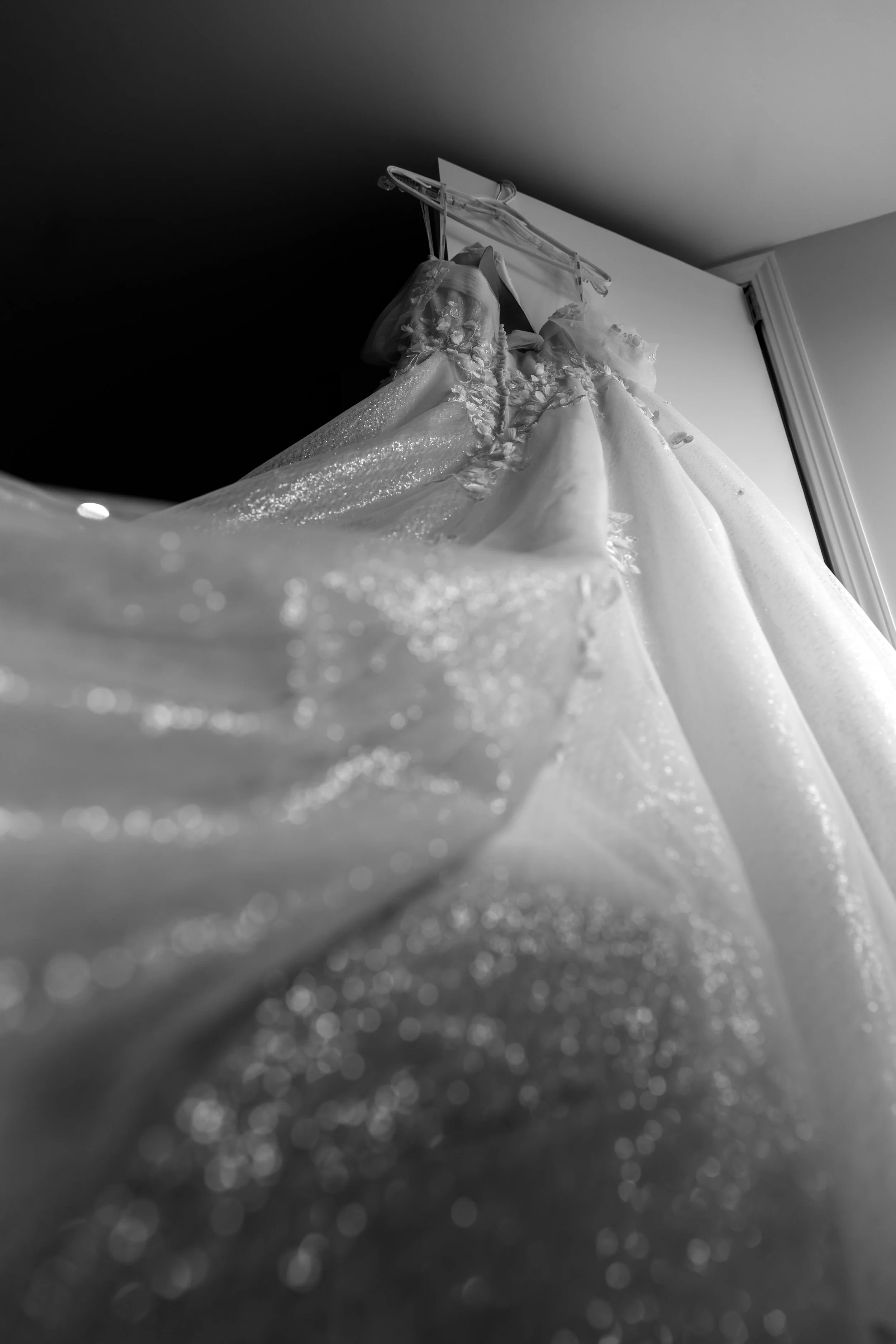 Wedding dress hanging on a door, captured in black and white from below.