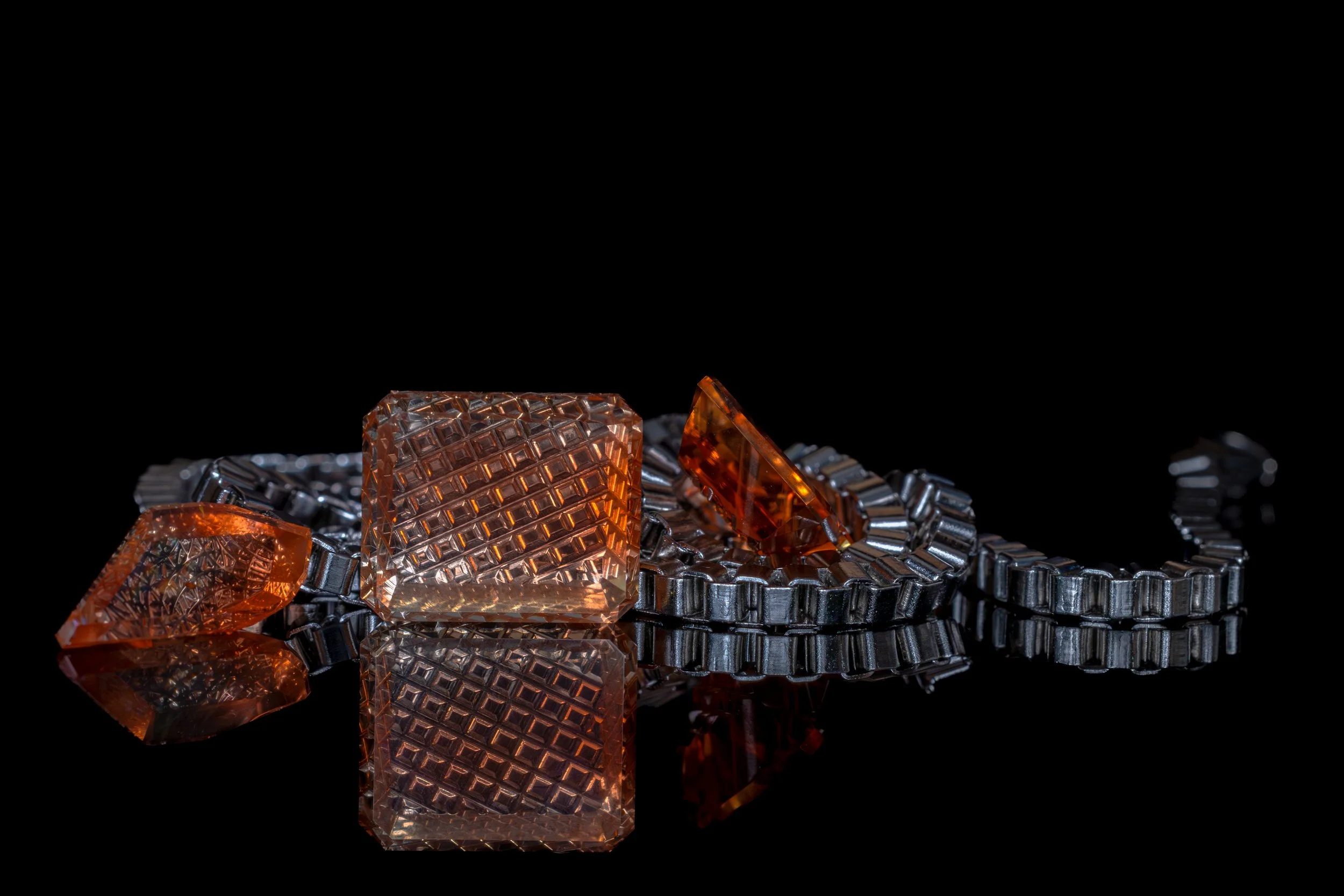 Close-up of amber-colored glass jewelry pieces with textured and smooth surfaces, placed on a reflective black surface.