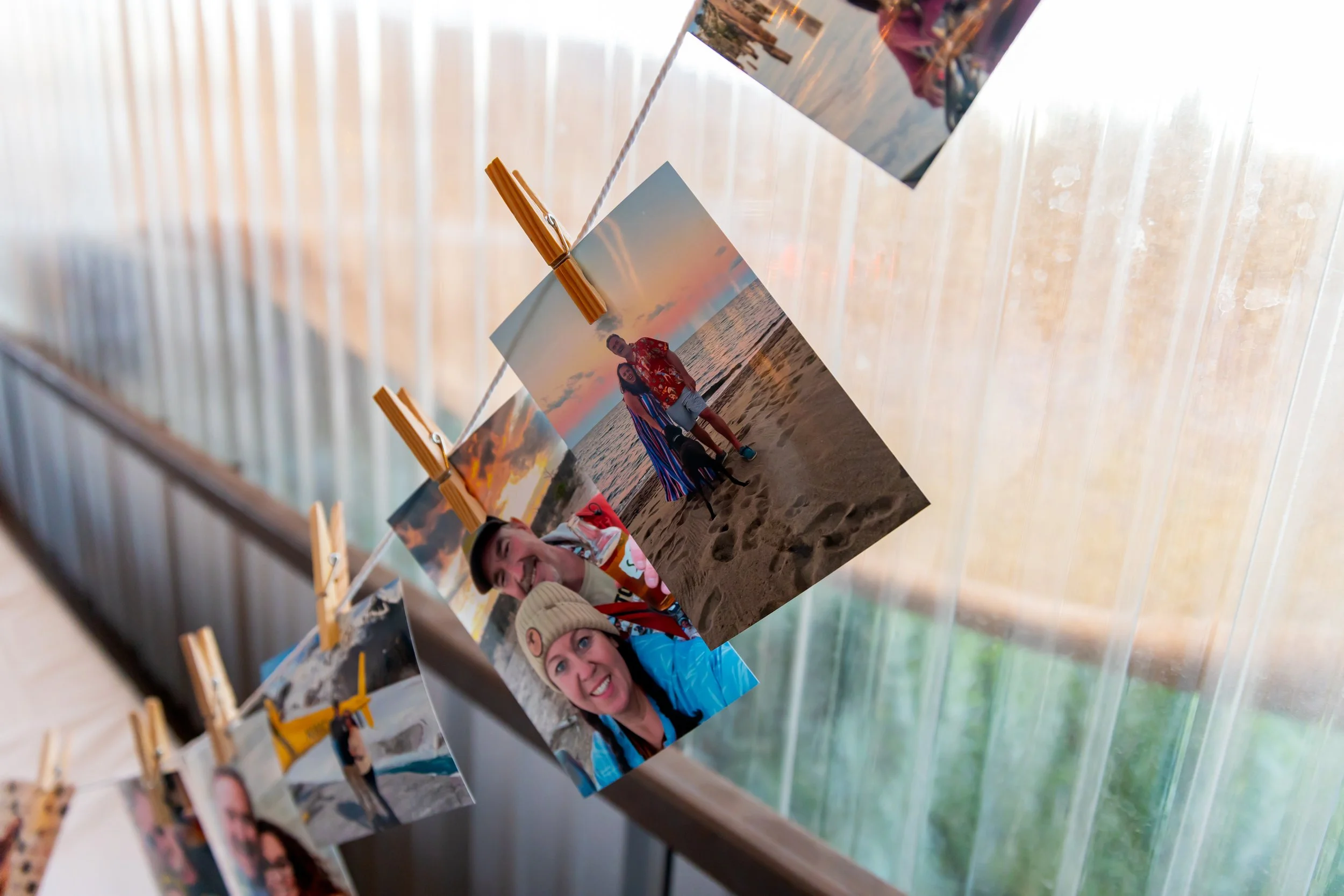 Photographs hanging on a string with clothespins, featuring people at a beach during sunset, some smiling at the camera.