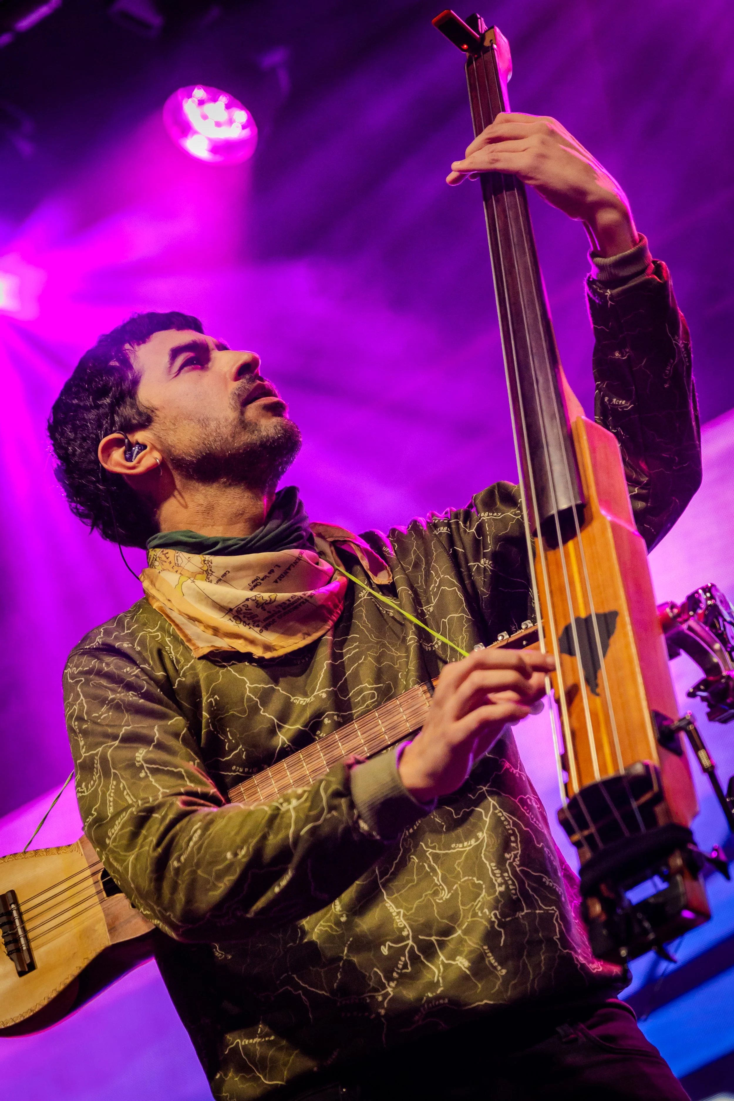 A man playing an acoustic guitar on stage, holding a console with purple and pink stage lights in the background.