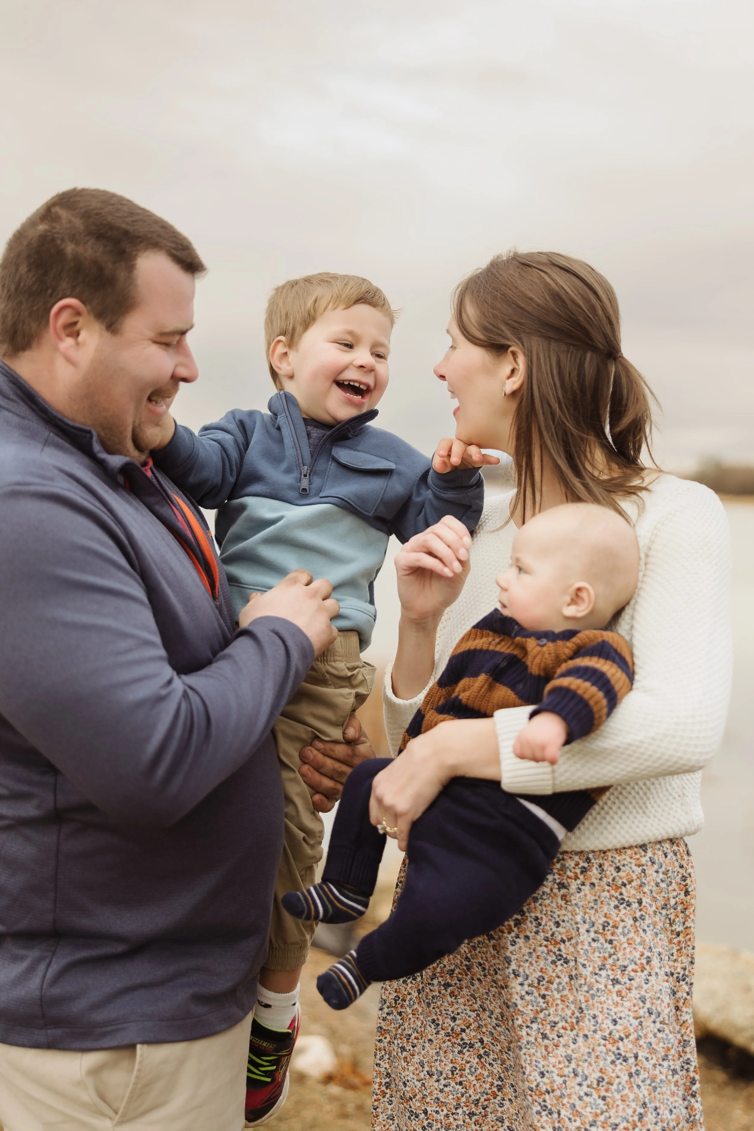 A family outdoors, with a man, a woman, and two young children, smiling and enjoying each other's company.