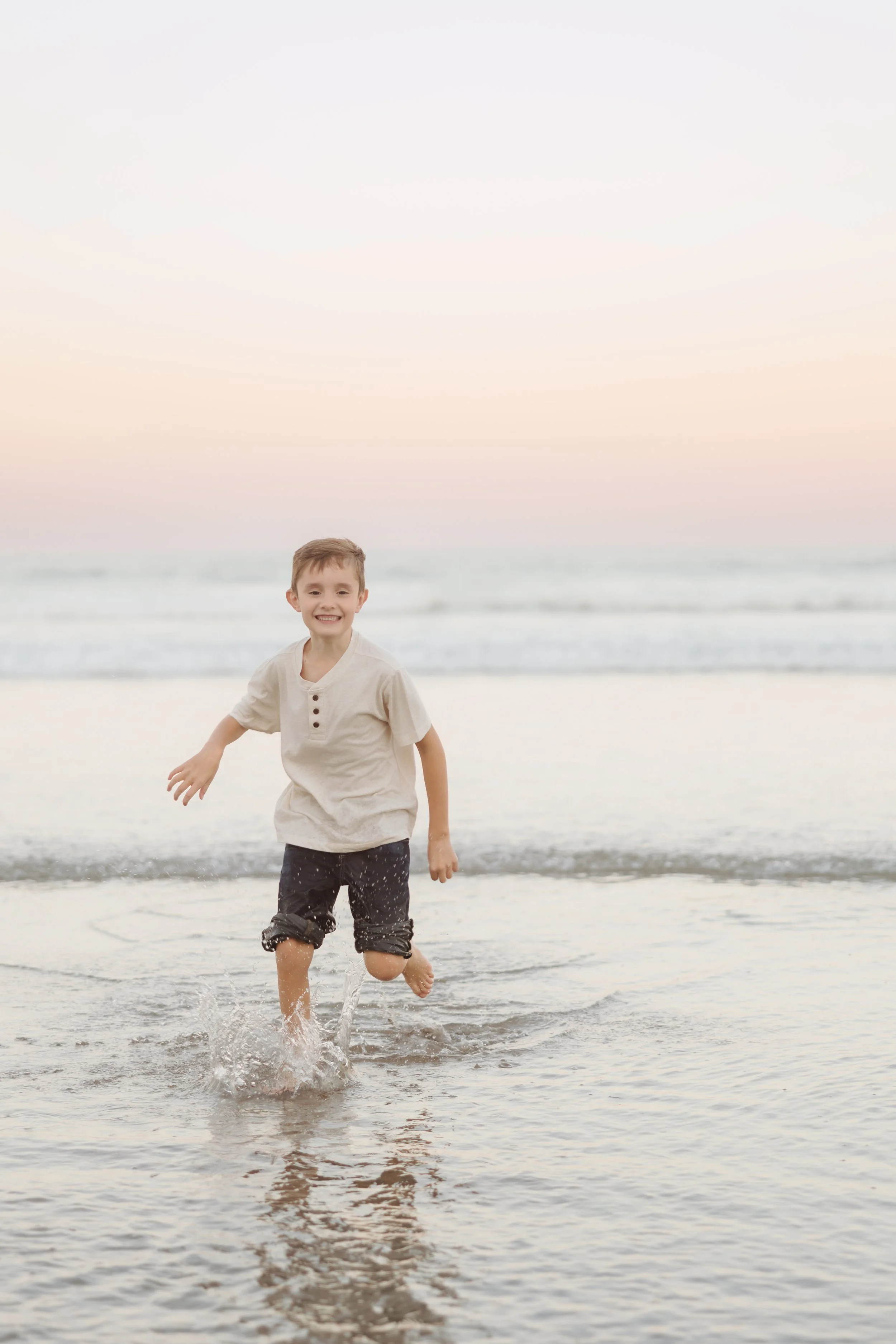 A young boy happily running in shallow ocean water at sunset on the beach.