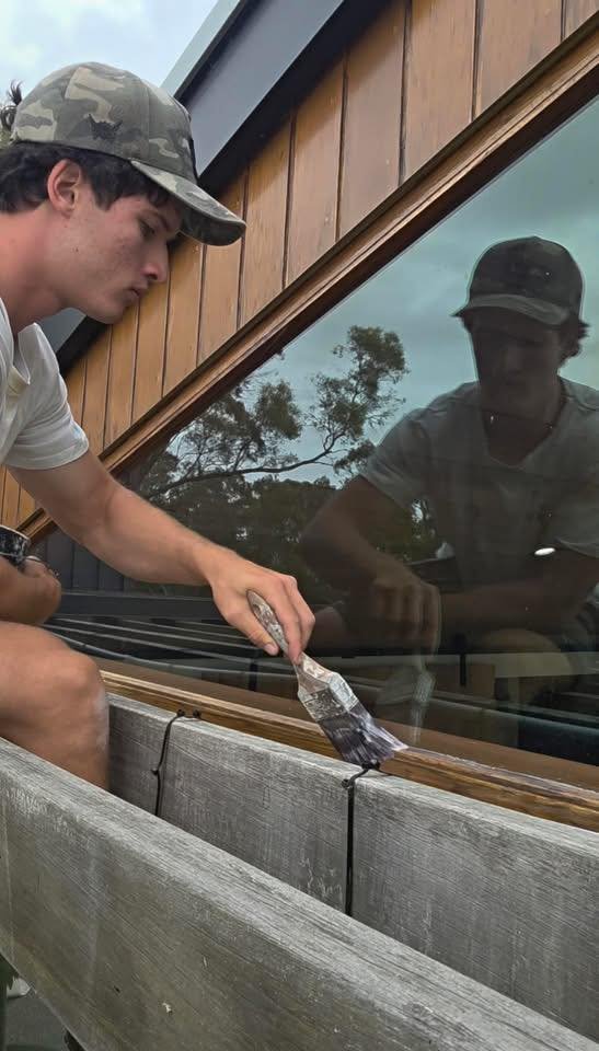 Man wearing baseball cap and painting a timber window frame