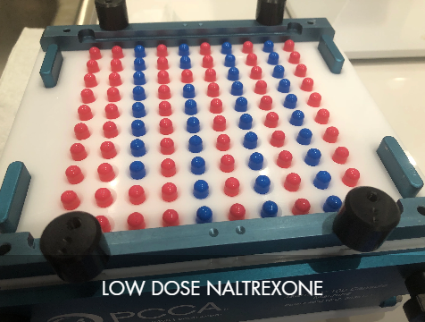 A low dose Naltrexone (LDN) game or testing device with red and blue pegs in a grid formation, enclosed in a blue frame with black wheels or rollers.