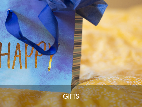 A birthday gift bag with a blue ribbon and striped paper, with the word 'HAPPY' partially visible, and wrapping paper with yellow and white patterns in the background.
