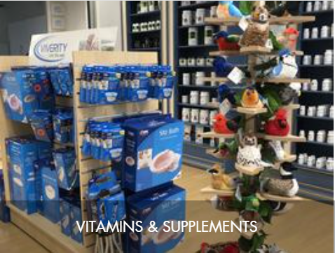 Display of vitamins and supplements on a store shelf with a decorative Christmas tree nearby.