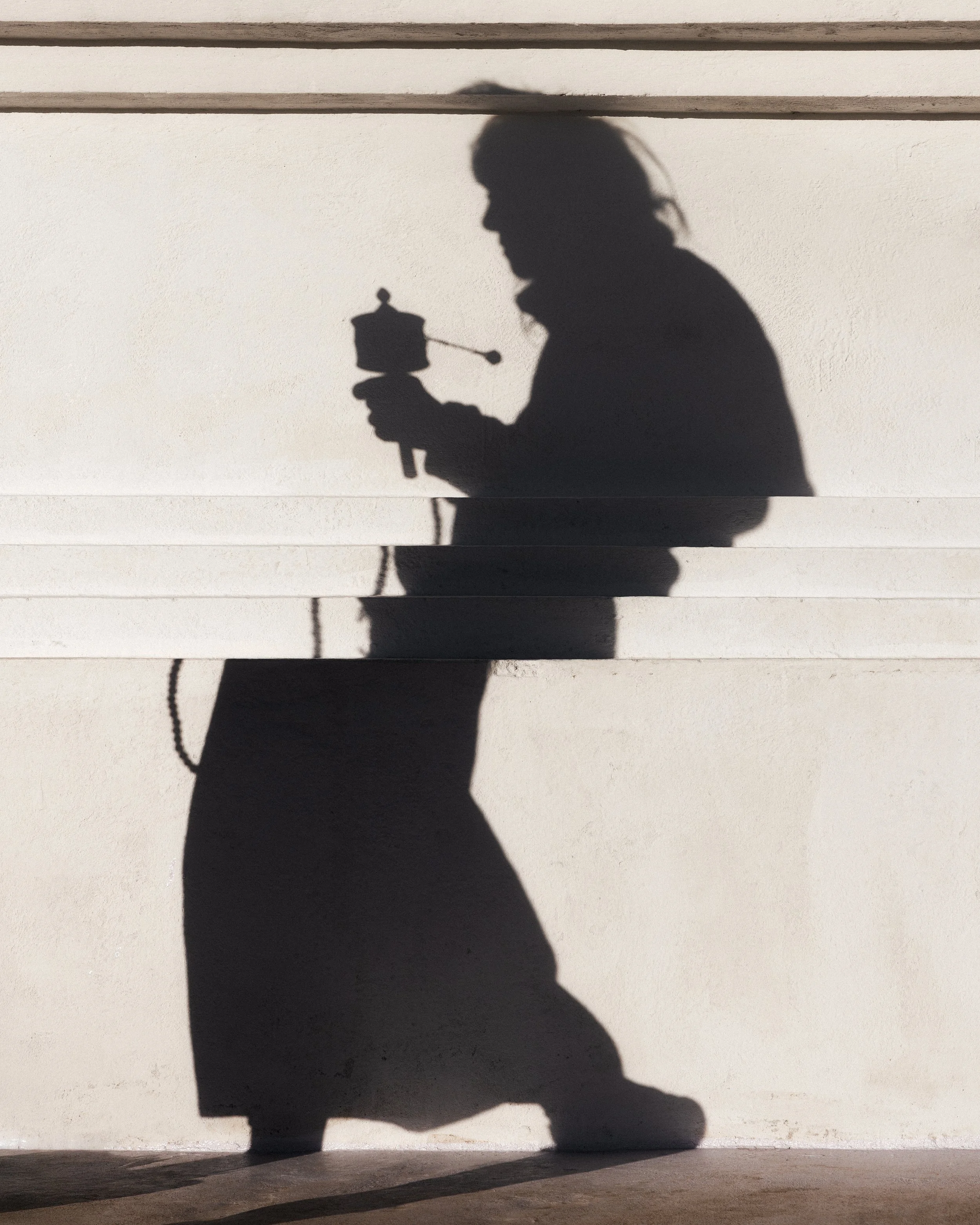 Shadow of a person holding a vintage coffee grinder, cast on a white wall.