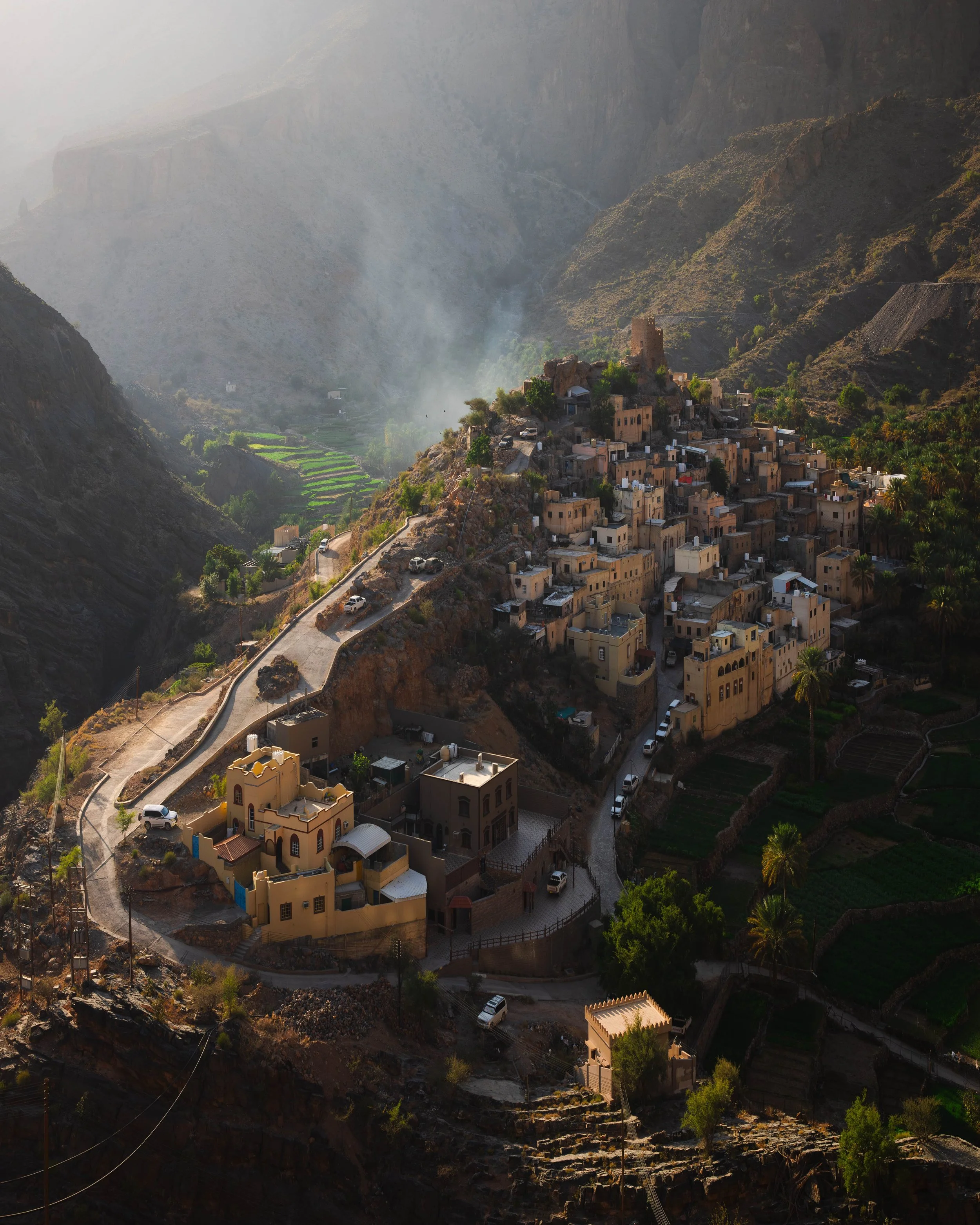 A village built on a hillside with winding roads, surrounded by mountains and green terraced fields.