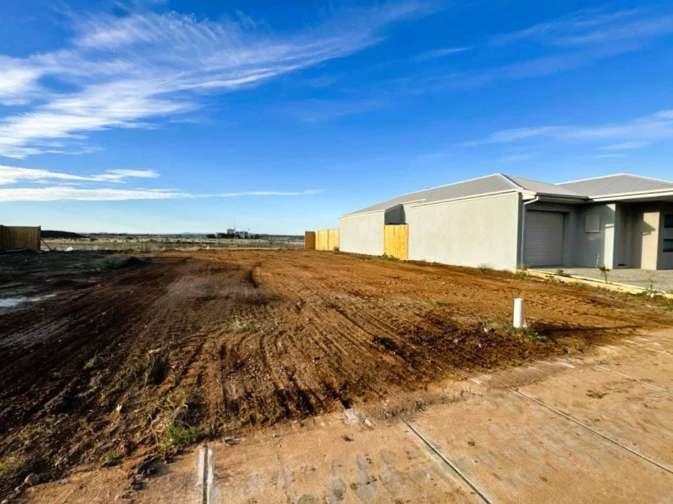 View of a partially developed residential area with a dirt lot and a newly built house on the right, under a blue sky with some clouds.
