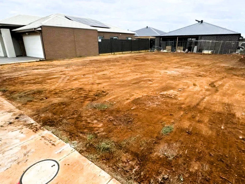 A cleared, dirt yard in a residential area with neighboring houses and fences in the background.