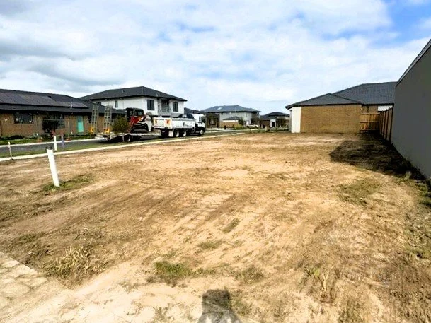 Empty dirt lot in a residential neighborhood with houses, trucks, and a cloudy sky.