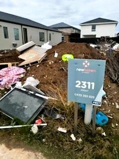 Construction site with debris and a sign that reads 'New Haven, 2311, 945-229-2500', nearby houses and a cloudy sky.