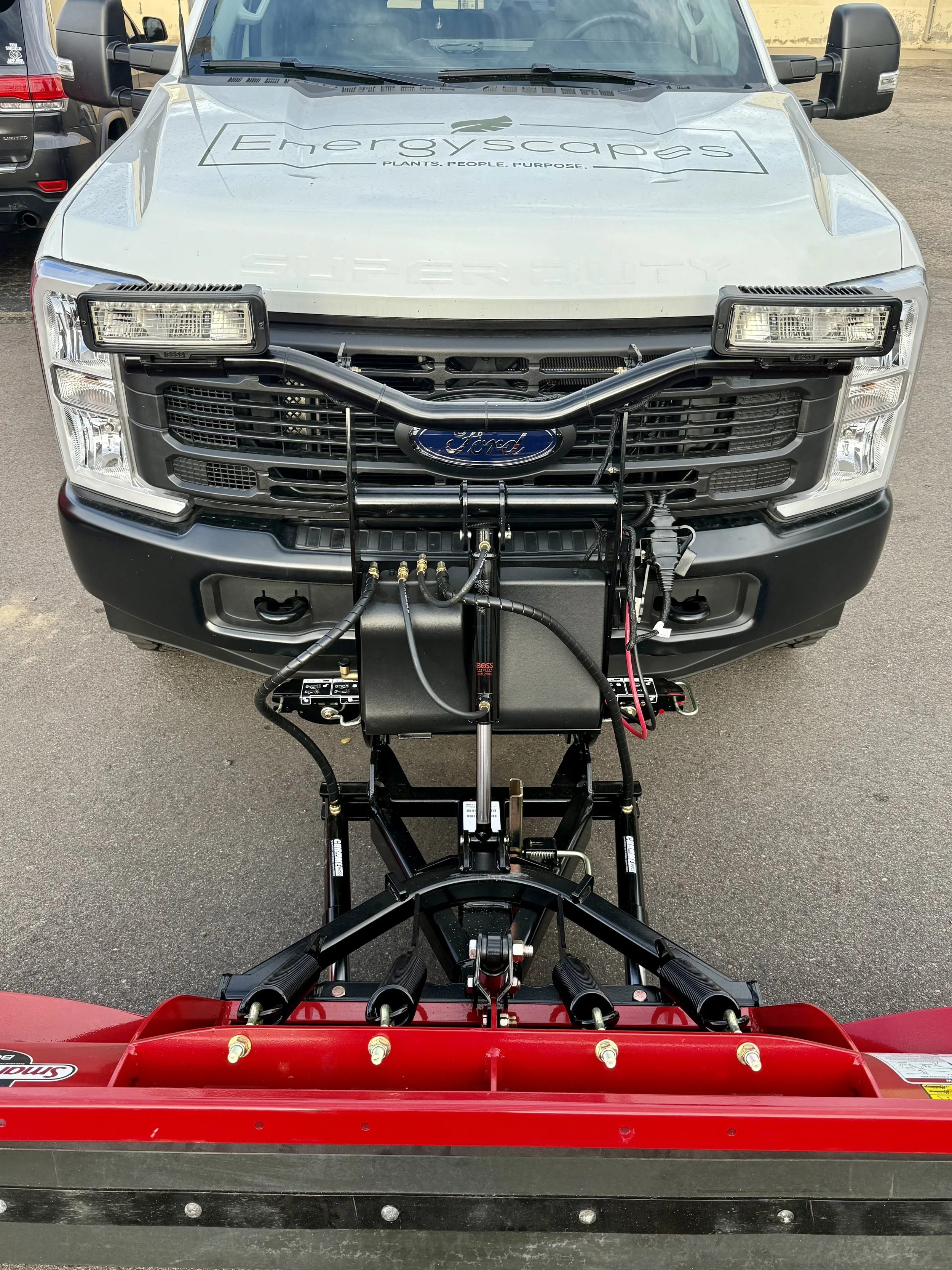 Front view of a Ford utility truck equipped with equipment for snow plowing or sanding, with a snow plow blade attached at the bottom.