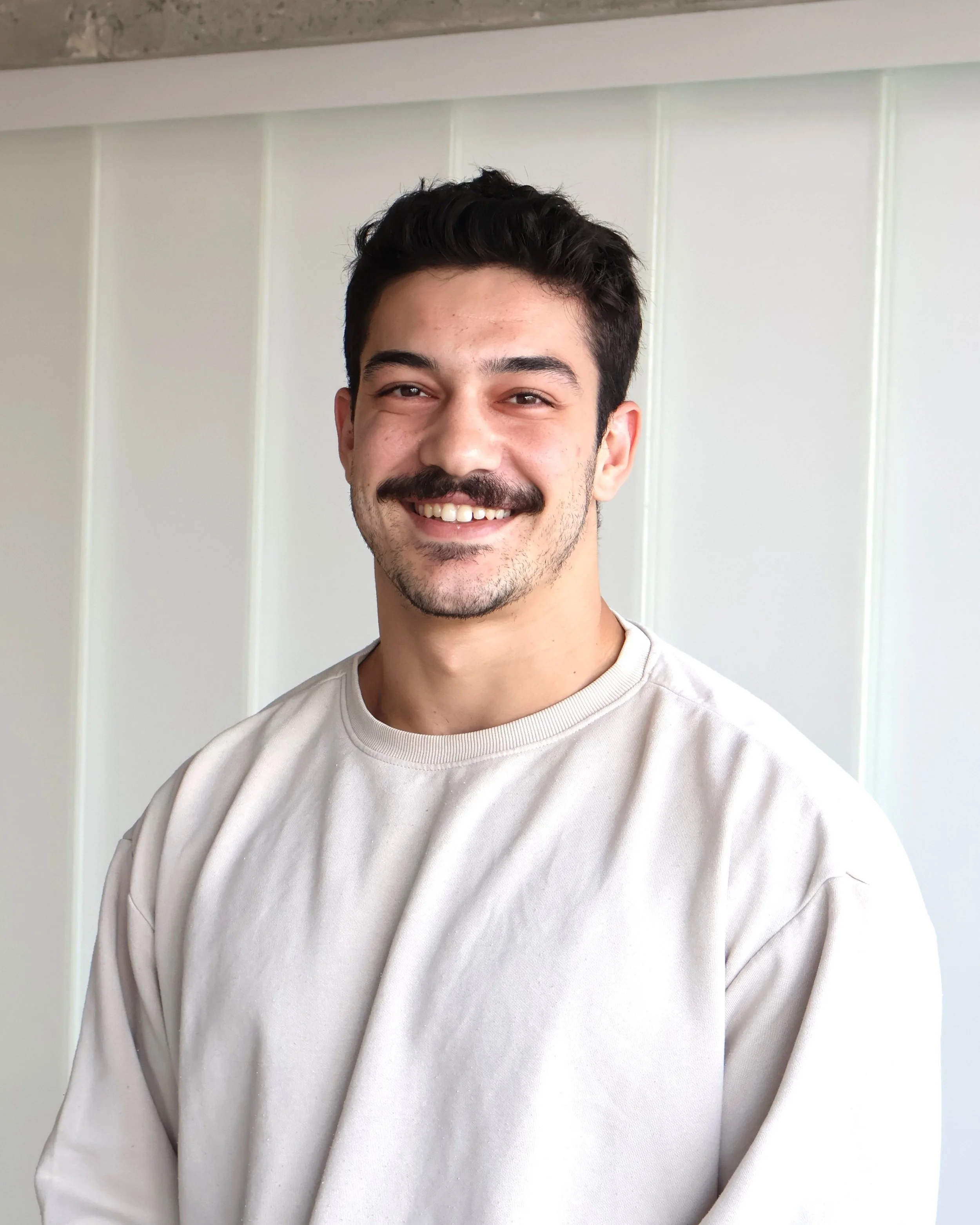 Mann in medizinischer Kleidung, lächelnd, vor neutralem Hintergrund.