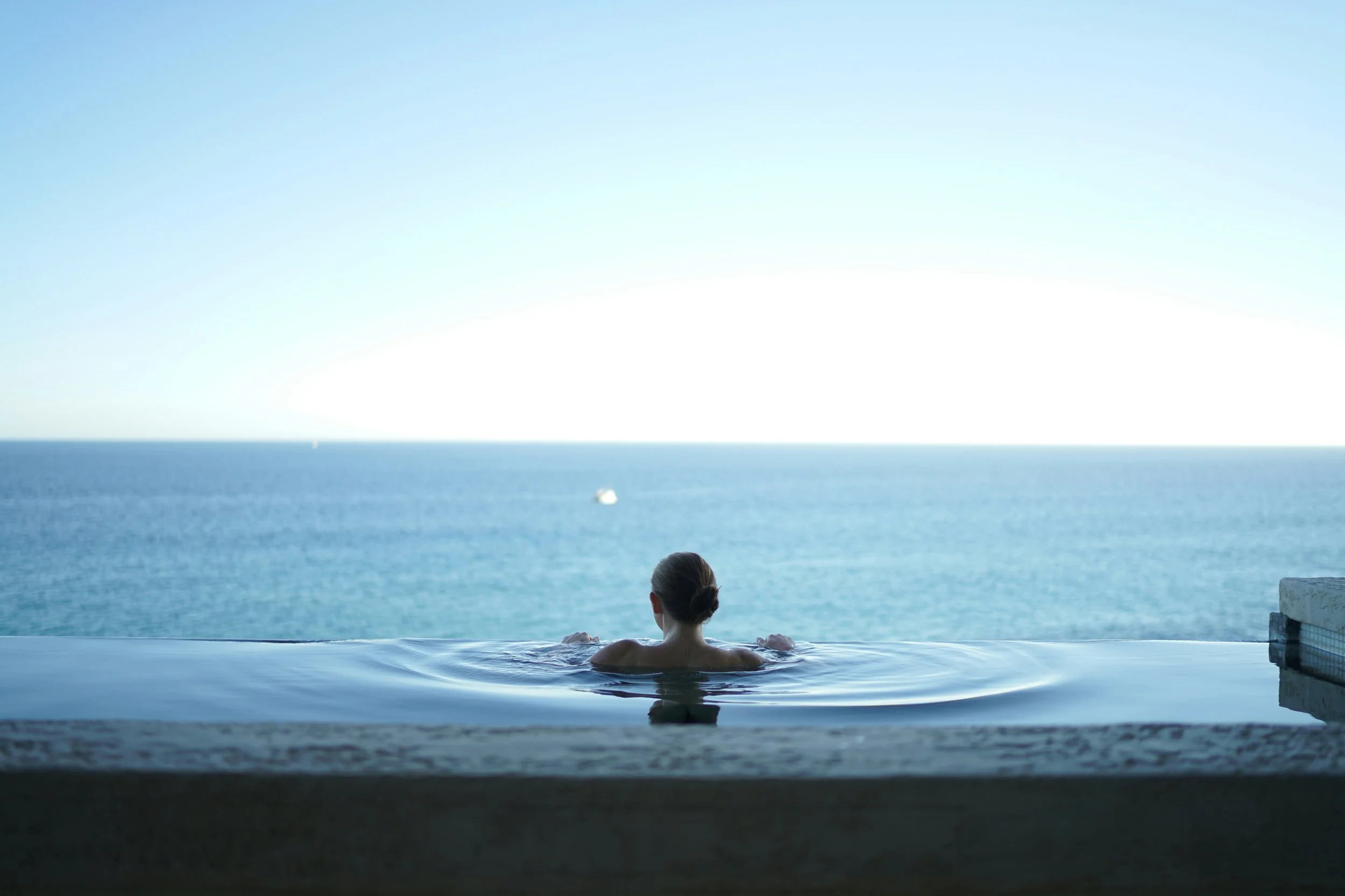 Person relaxing in an infinity pool overlooking the ocean at sunset.