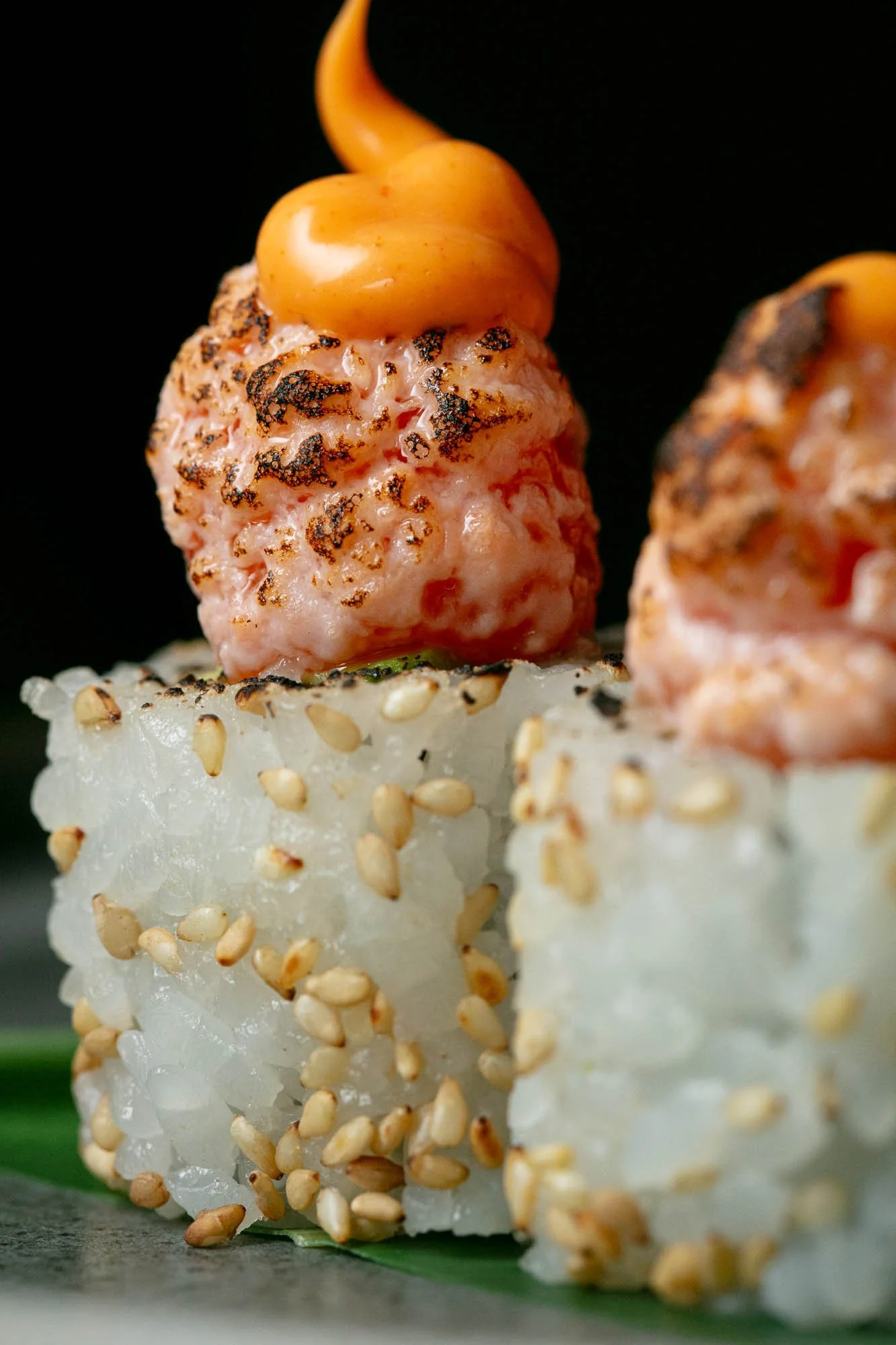 Close-up of sushi rolls topped with grilled tuna and spicy mayo, garnished with sesame seeds on the rice portion at Ayllu Restaurant in Central London.