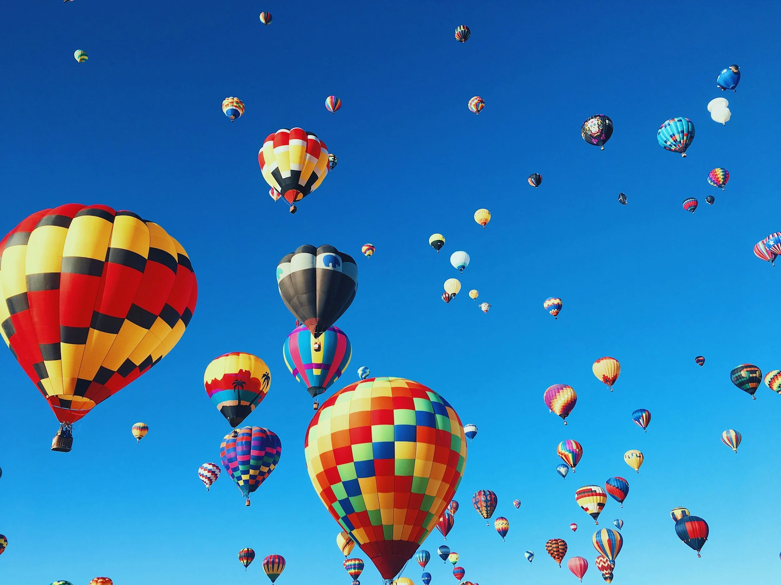 Numerous colorful hot air balloons floating in a clear blue sky.