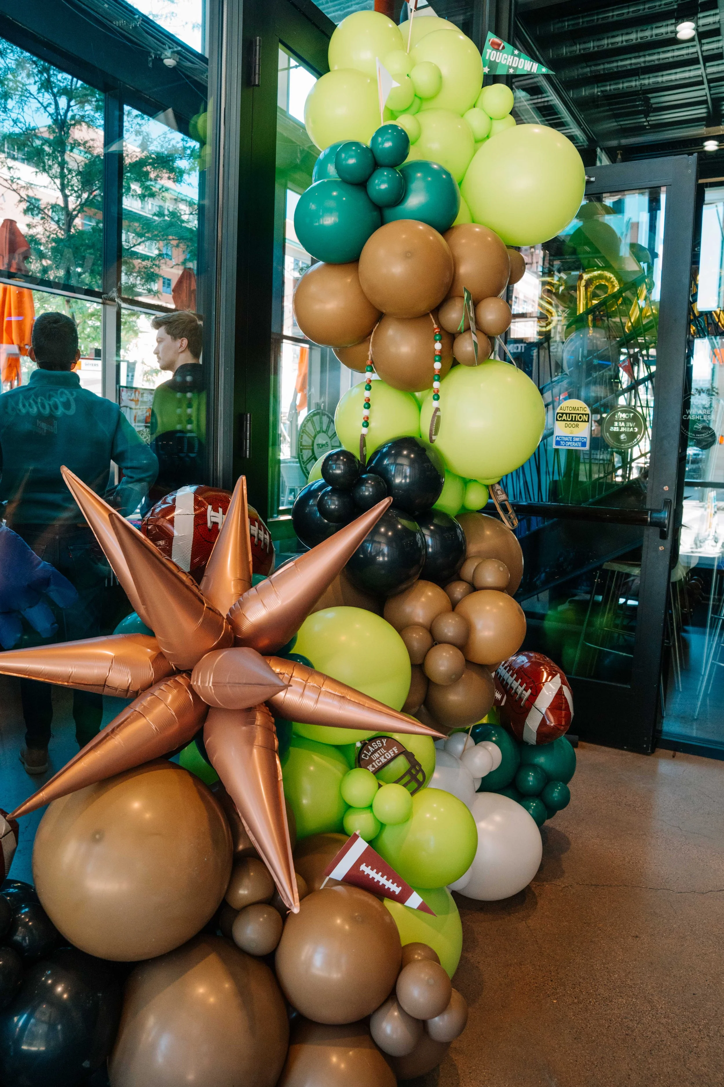 Decorative balloon arrangement in green, brown, black, and white balloons based on a football theme, with football-shaped balloons and a sign that says 'Touchdown'.
