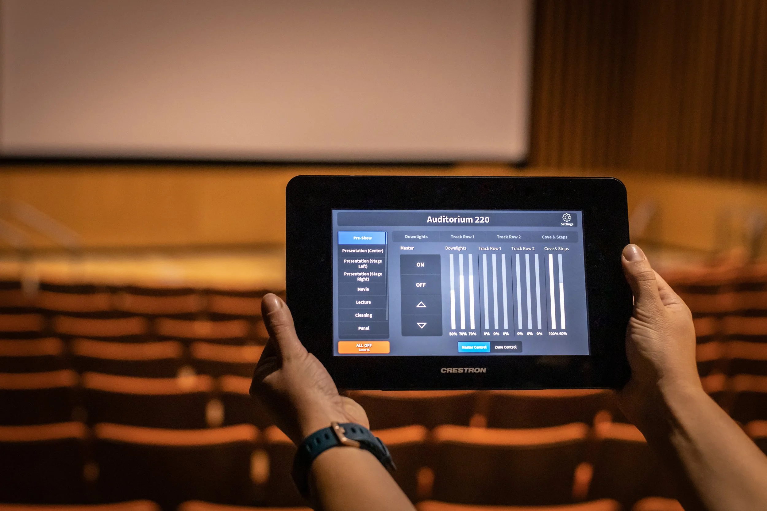 An auditorium with rows of orange seats and a wooden-paneled wall at the front.