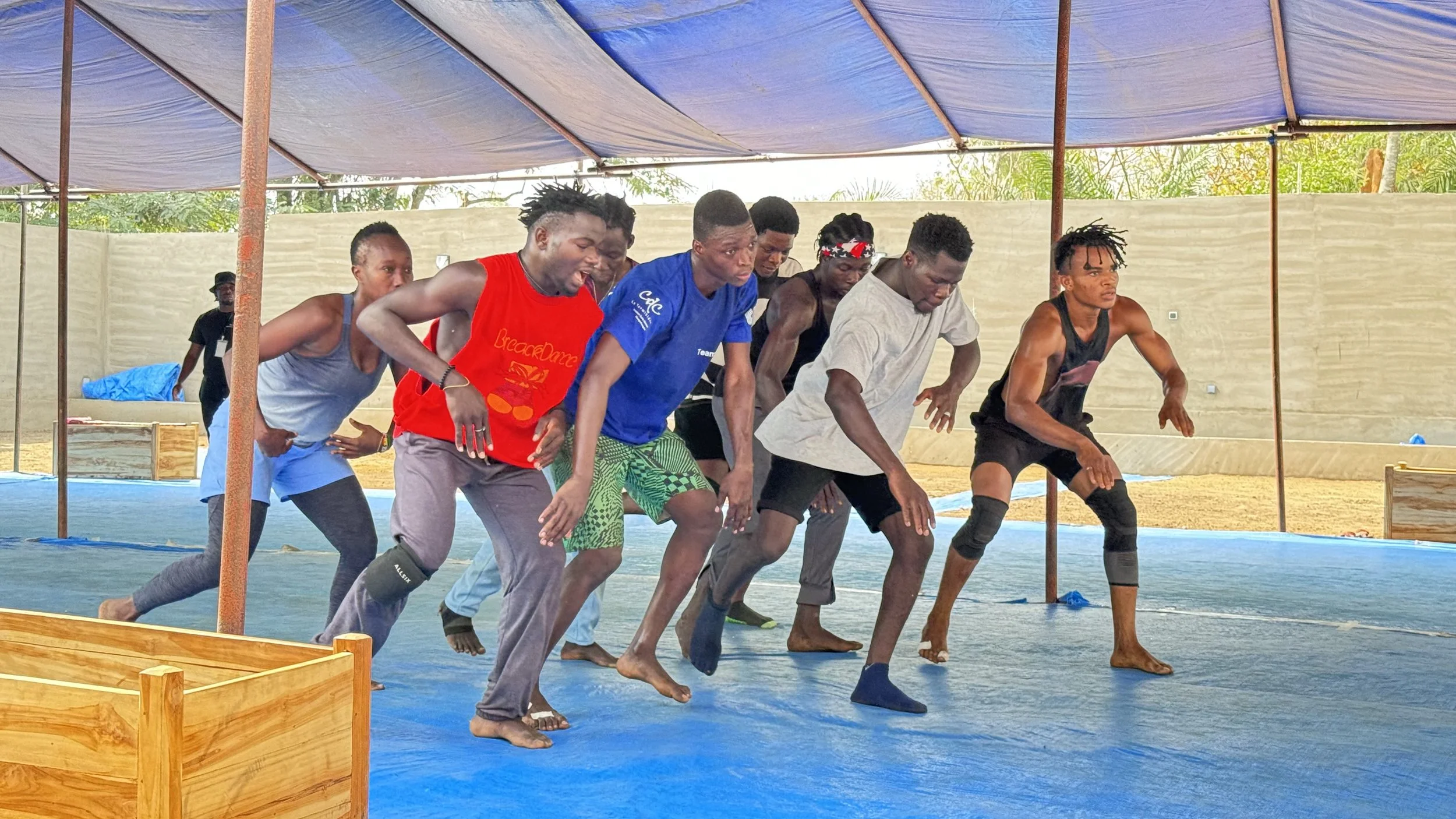 Groupe de personnes pratiquant la danse ou un entraînement en intérieur sous une grande tente, avec un sol en plastique bleu.