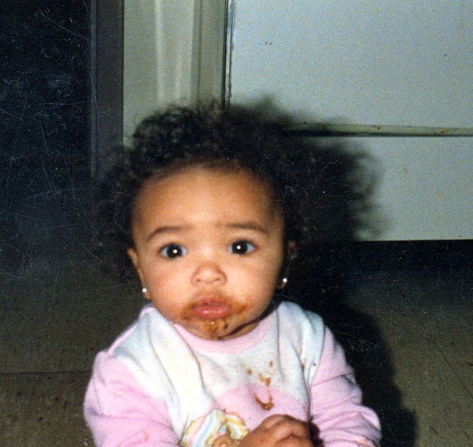 An image of LinkTech founder, Tia Kleckner, as a baby. Curly hair and earrings, looking at the camera with a surprised or curious expression, with some food or crumbs on her face and clothing.