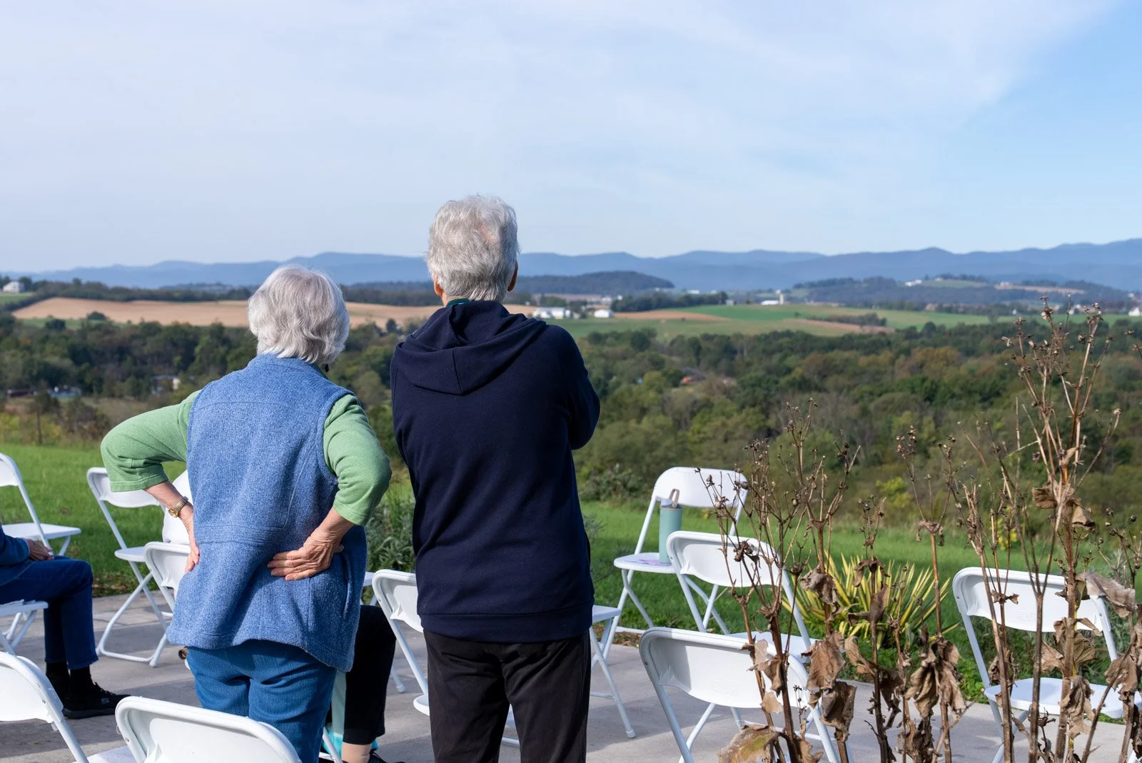 Two yoga participants stand beside folding chairs at VMRC’s farm, looking out over fields and mountains in Harrisonburg, VA.