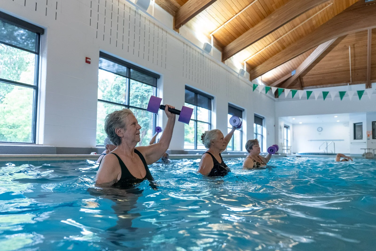 VMRC Wellness Center members doing aqua aerobics with hand weights in the indoor pool.