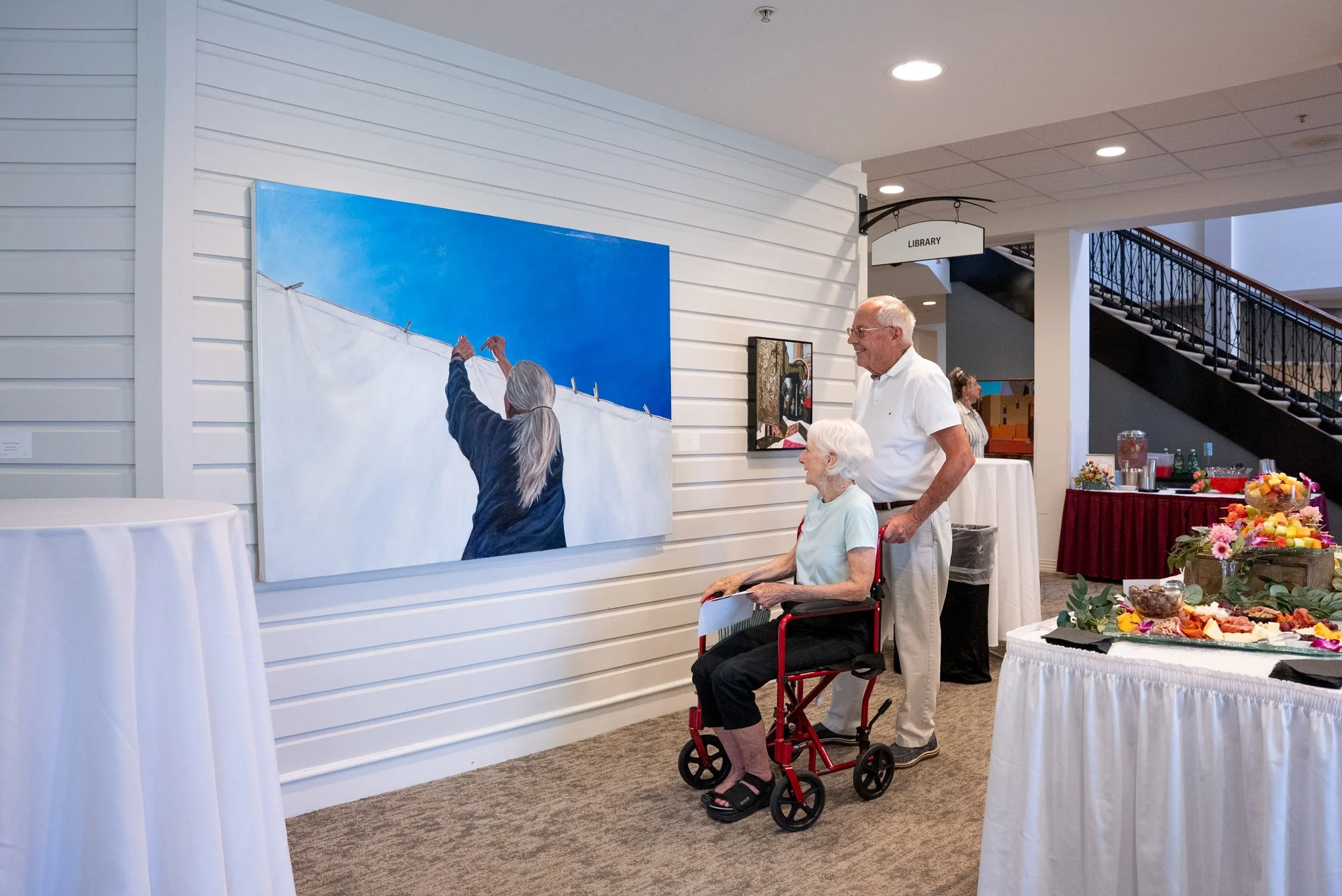 an older couple admiring a piece of artwork at the 2026 juried art exhibition