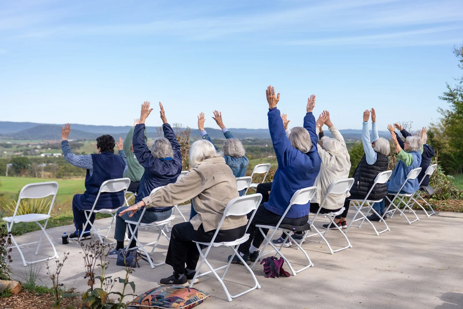 Older adults raise their arms during outdoor chair yoga at VMRC’s farm, overlooking fields and mountains in Harrisonburg, VA.