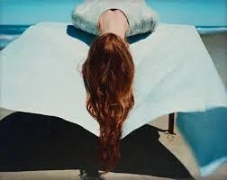 A person lying face down on a bed with red long hair covering her face