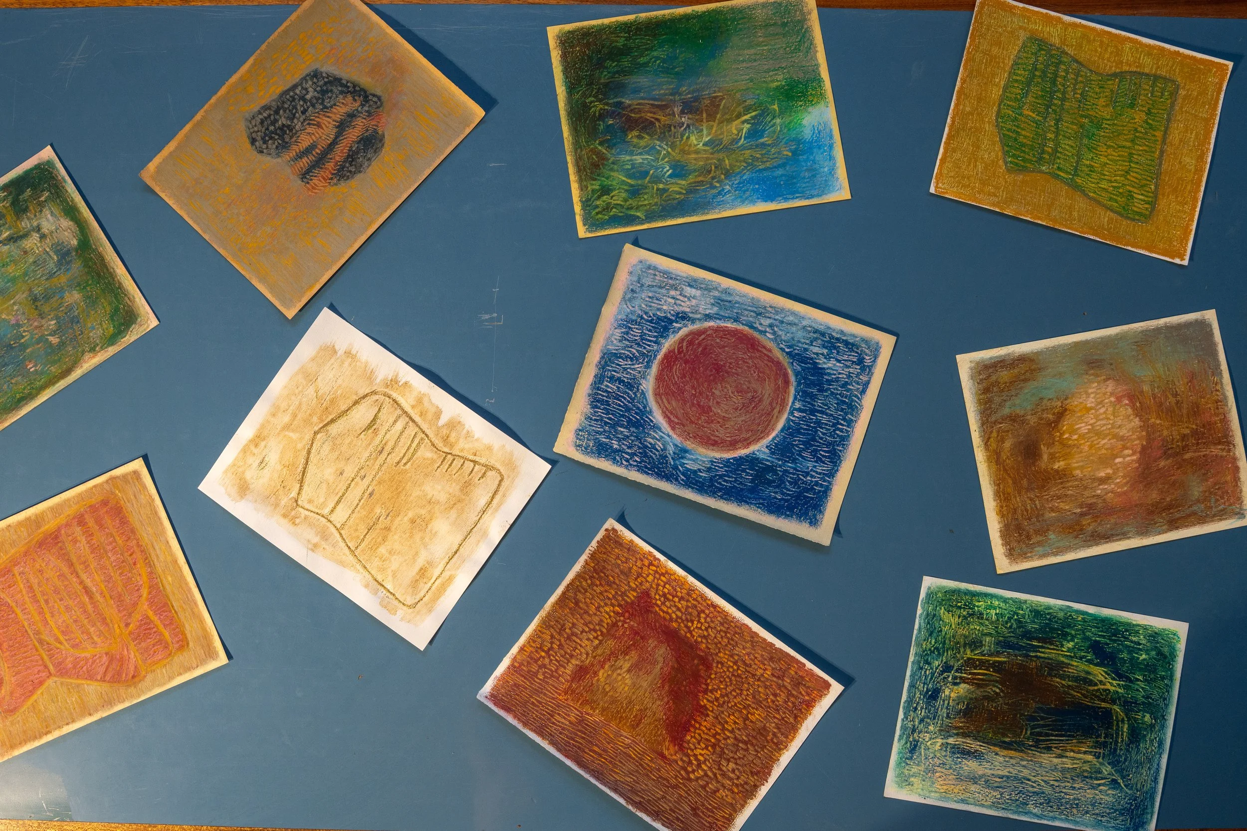 Colorful abstract drawings on small paper sheets scattered on a blue surface.