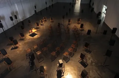 Empty concert hall with scattered chairs and music stands, stage lights illuminating the space.
