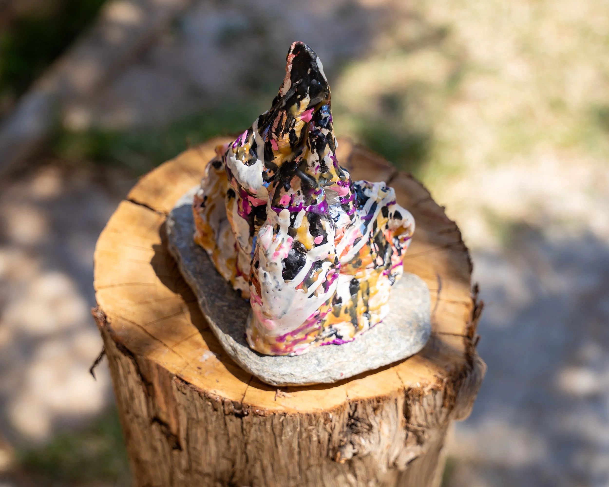 Colorful art work on a sliced log in an outdoor setting. Abstract ceramic sulpture by Finnish artist Satu Metsola