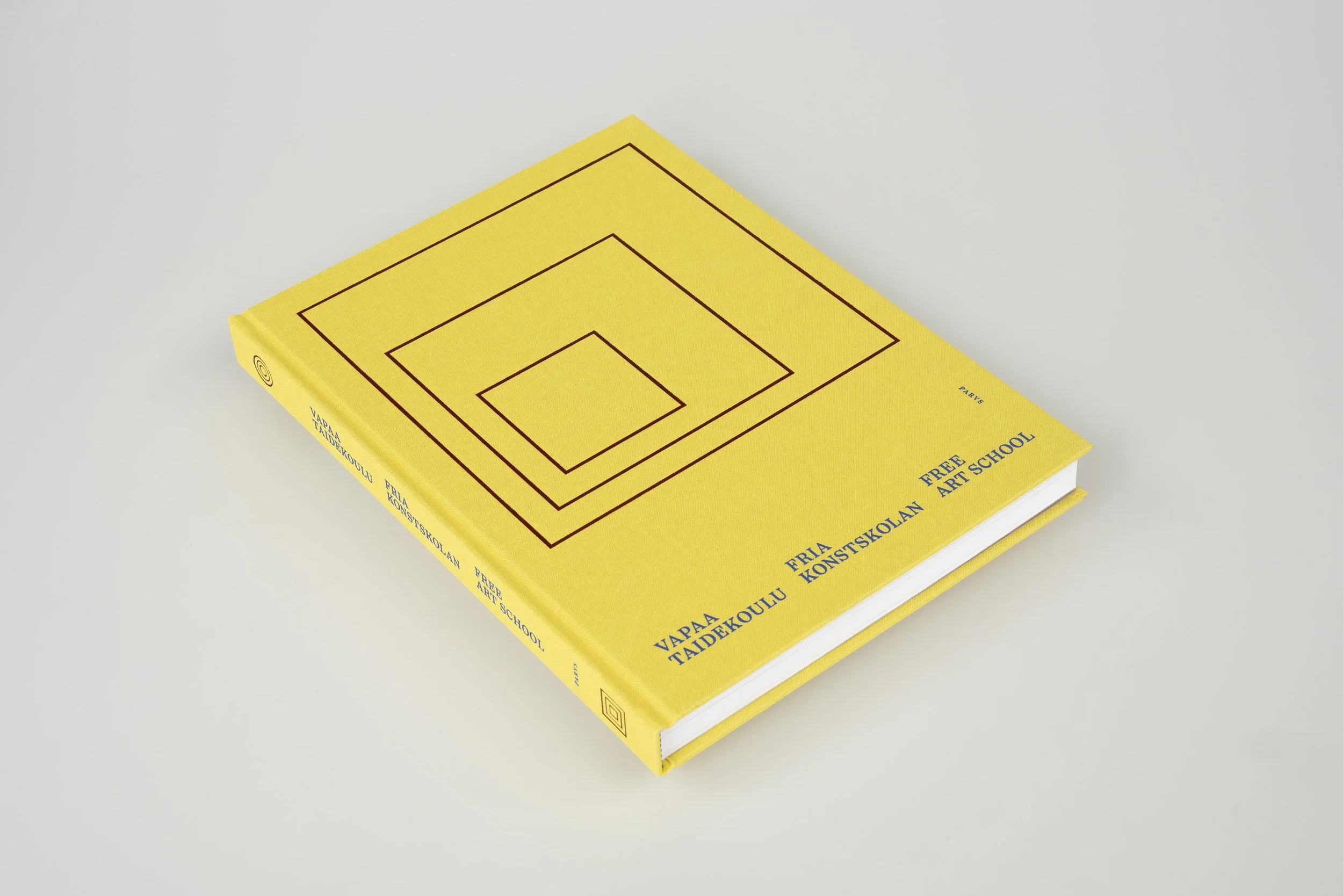 A yellow hardcover book titled 'Vapaa Taidekoulu' with black geometric lines on the cover, placed on a plain white surface.