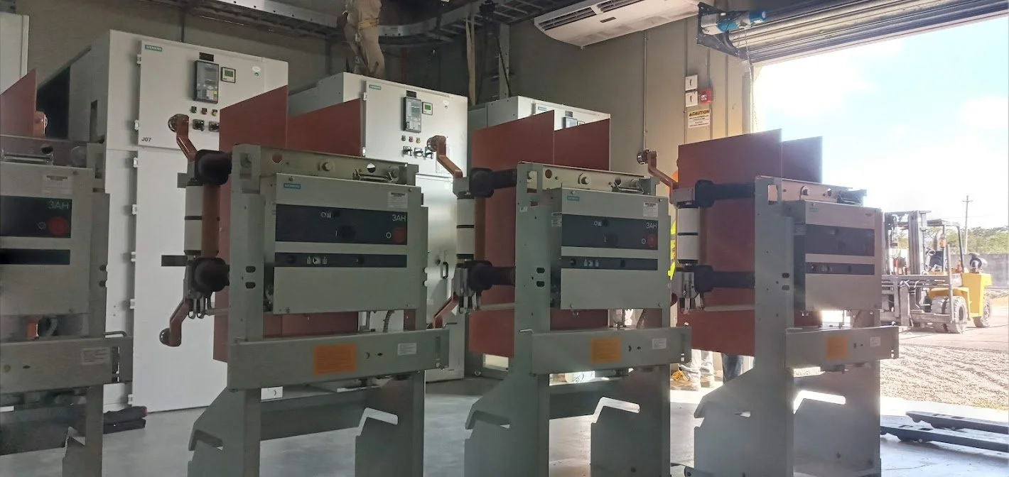 Electrical equipment and transformers inside a warehouse with an open garage door showing a forklift outside.