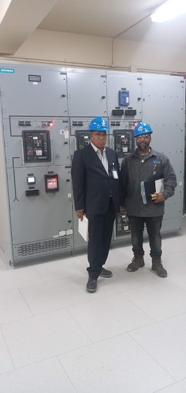 Two men, which includes Leecorp Ltd's Founder and CEO, Francois Lee, wearing blue safety helmets standing in front of electrical circuit panels inside an industrial facility.