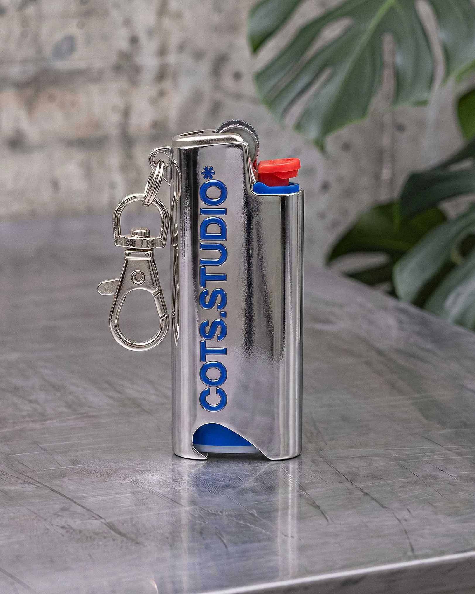 COTS LIGHTER HOLDER cromato con logo COTS.STUDIO blu, moschettone e accendino BIC Mini inserito