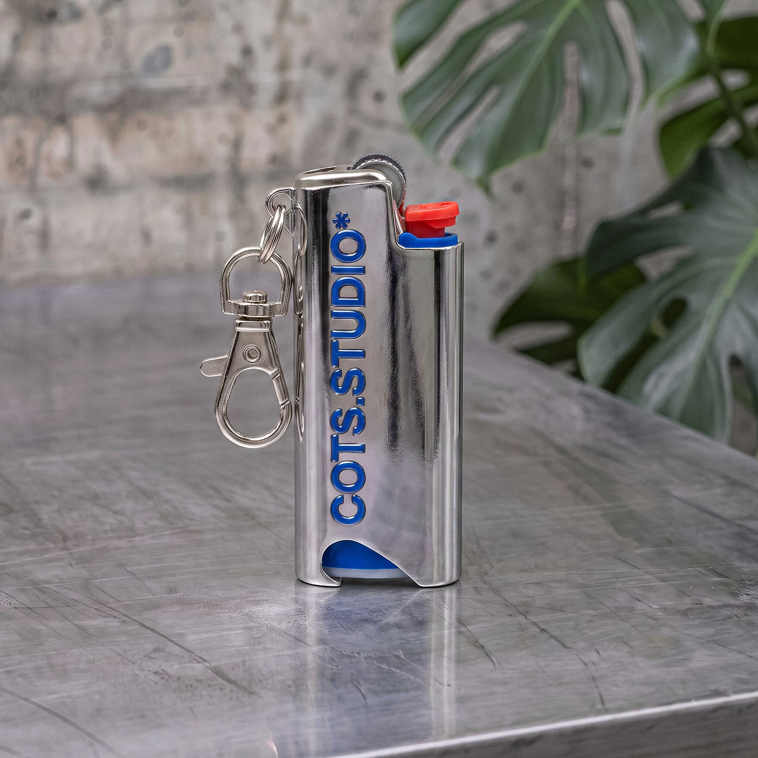 COTS LIGHTER HOLDER cromato con logo COTS.STUDIO blu, moschettone e accendino BIC Mini inserito