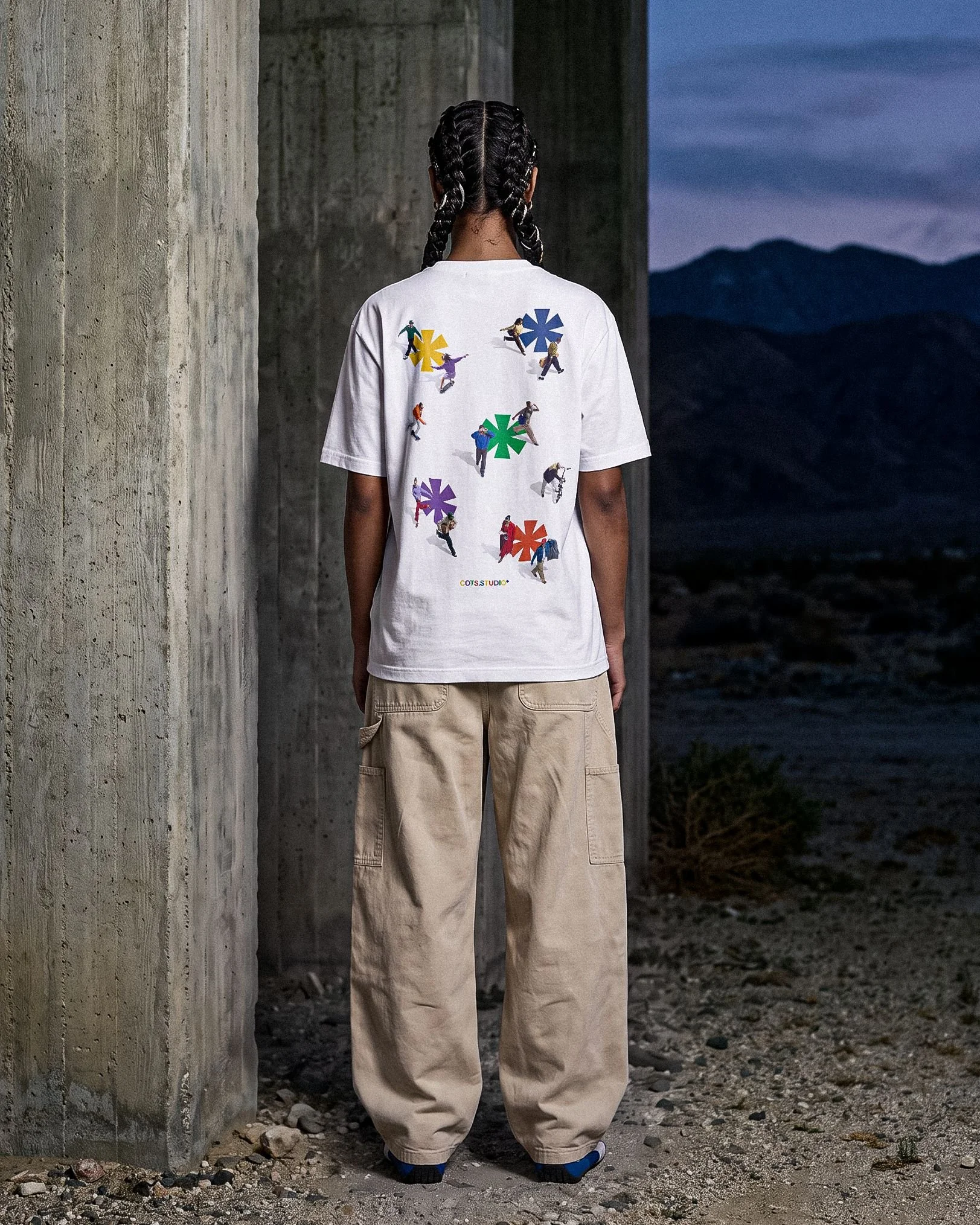 EVERYONE TEE COTS.STUDIO bianca indossata, vista posteriore con artwork di figure e asterischi multicolore