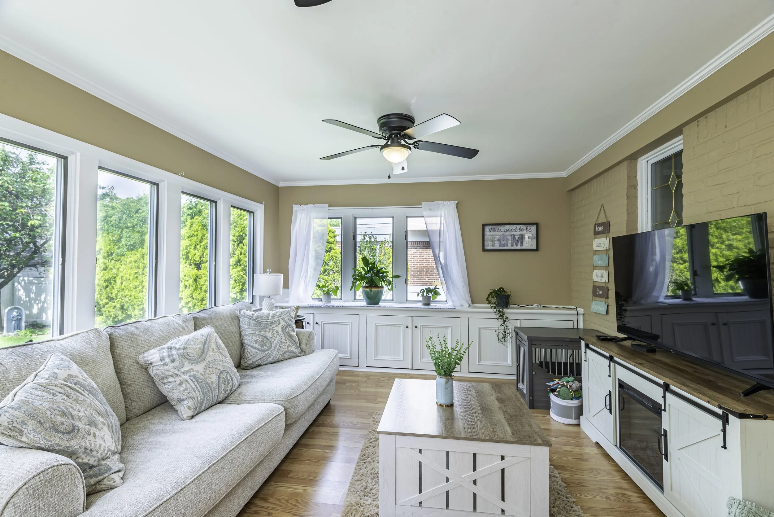 Spacious family room featuring hardwood flooring, neutral tones, large windows, ceiling fans, and professionally staged furnishings.