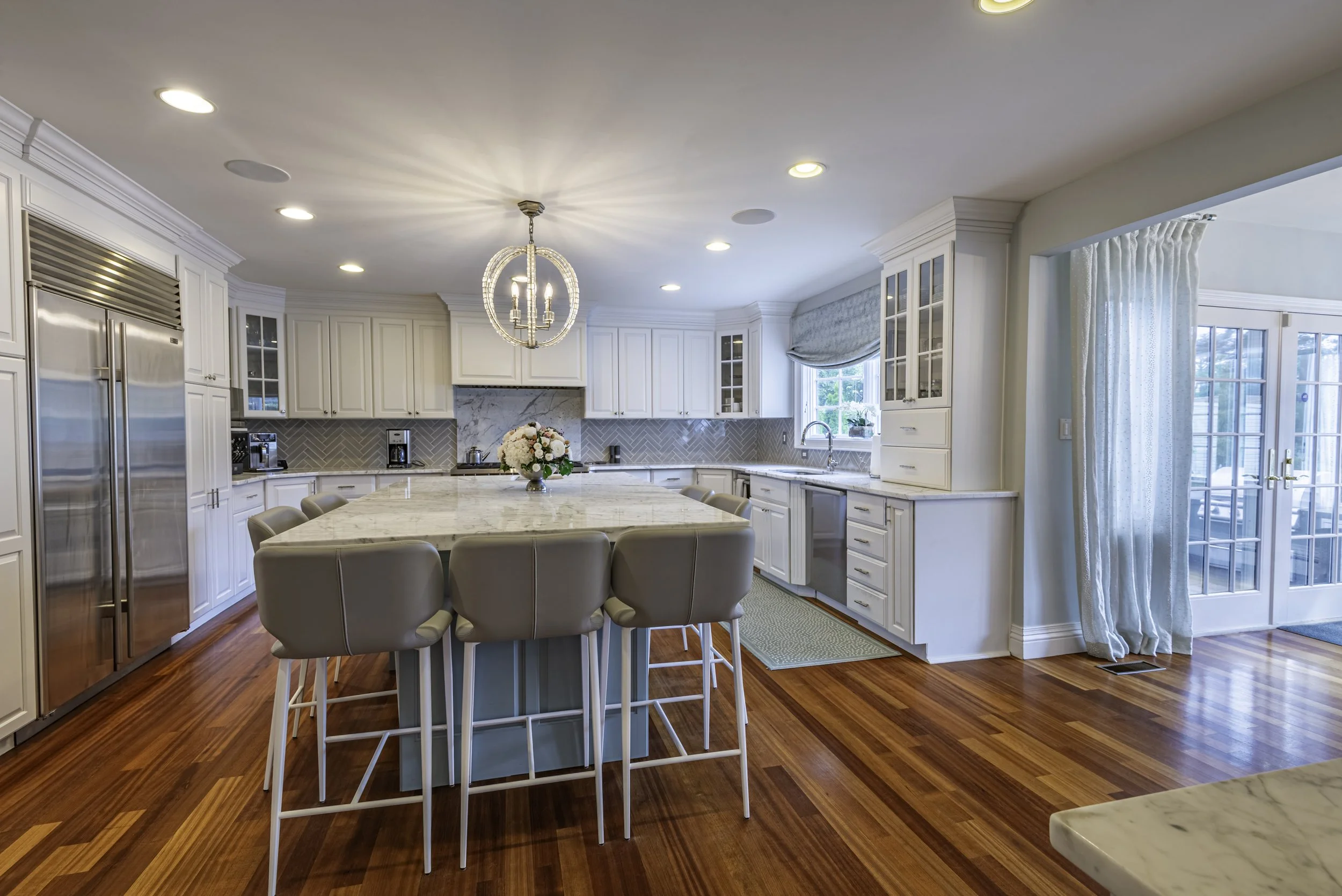 Luxury white kitchen interior with marble island, hardwood floors, modern lighting, and natural window light captured for real estate photography in New York.